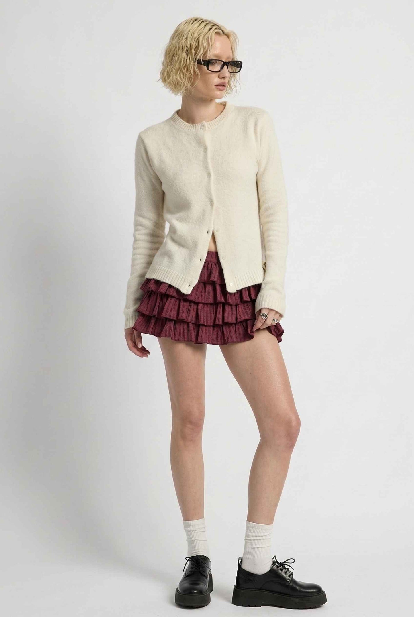 Model wearing Penelope Top in Off White Soft Wool-Blend Crew Neck Button-Up Cardigan with ruffle mini skirt and loafers