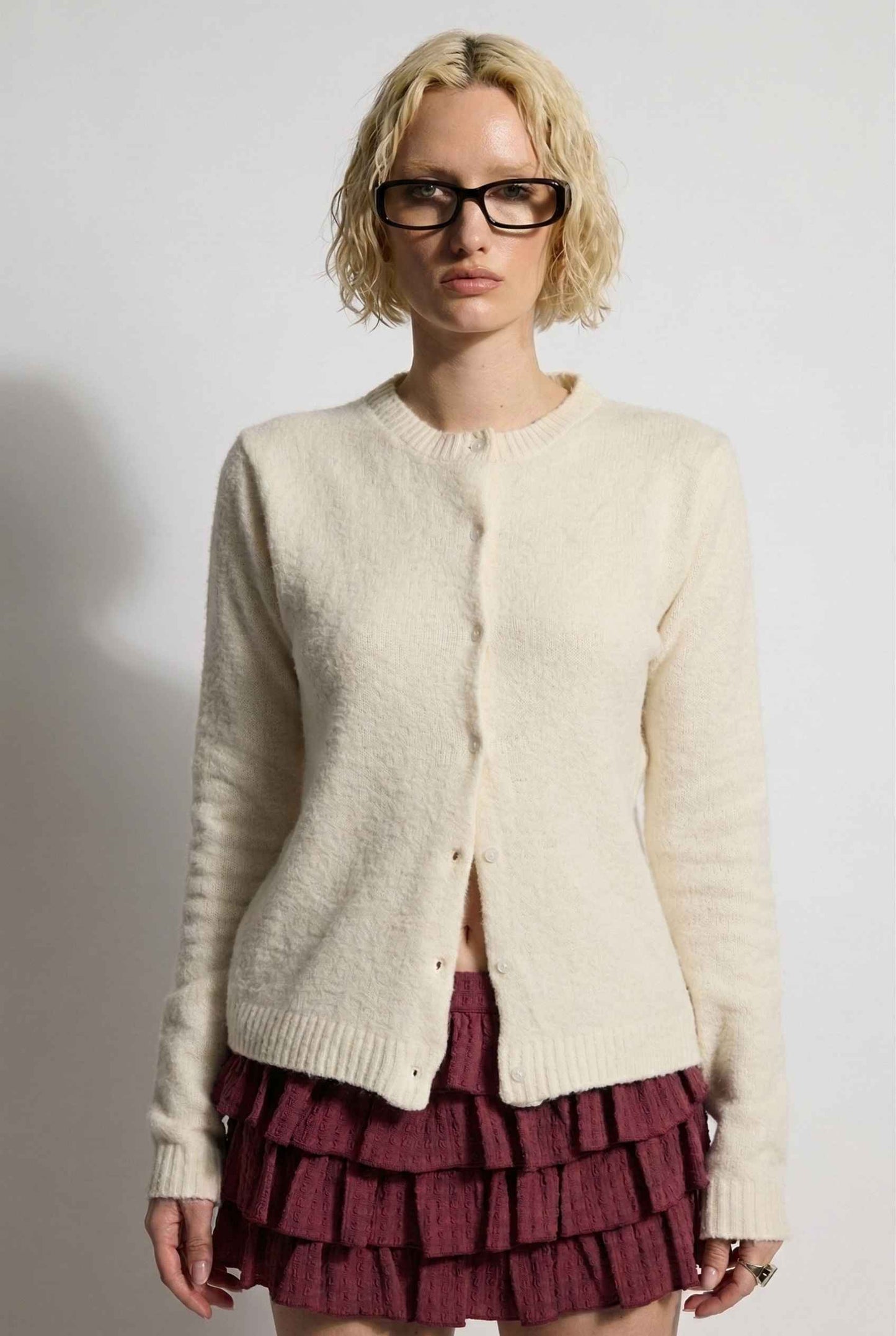 Model wearing Penelope Top in Off White Soft Wool-Blend Crew Neck Button-Up Cardigan with ruffle mini skirt