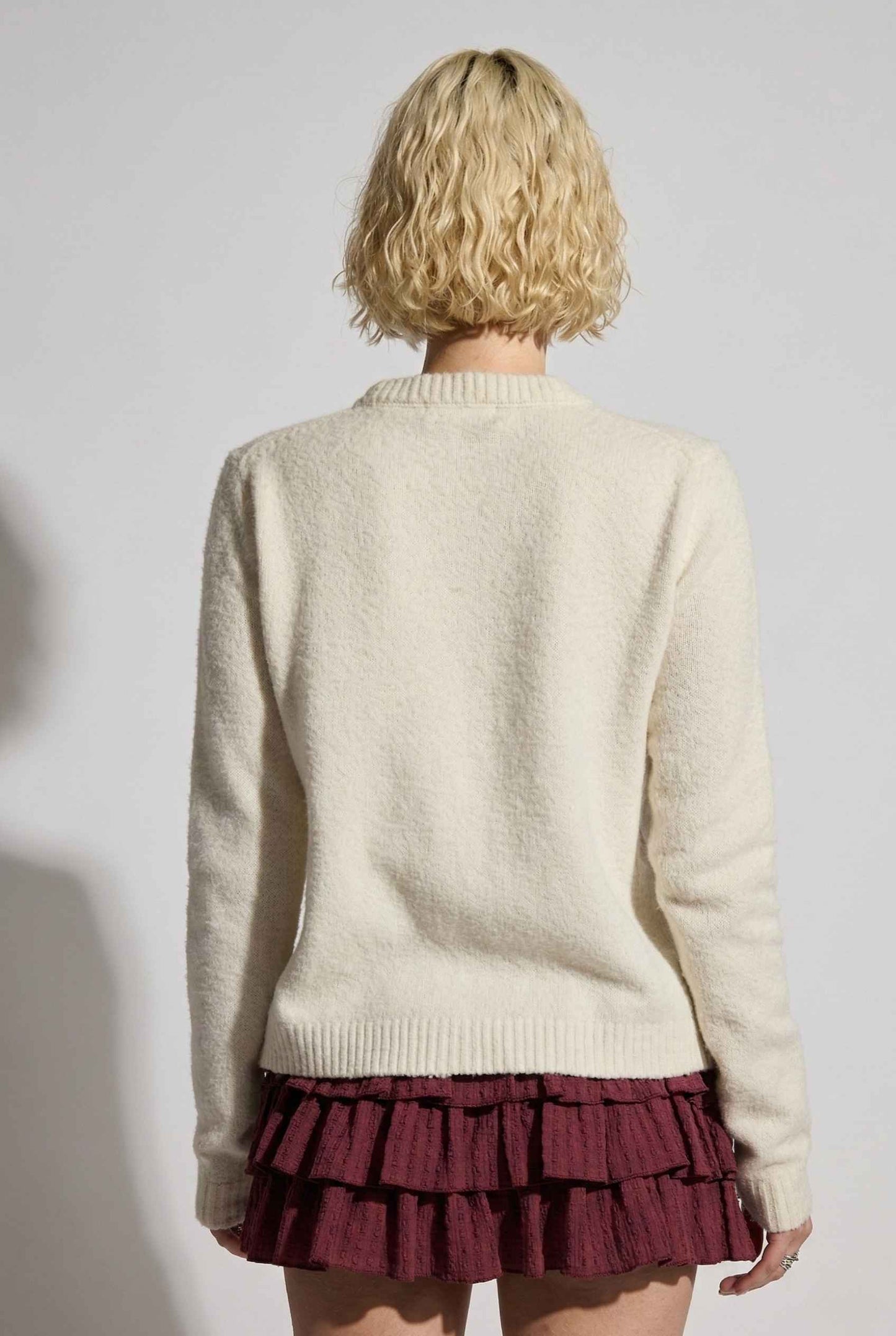 Model wearing Penelope Top in Off White Soft Wool-Blend Crew Neck Button-Up Cardigan with ruffle mini skirt