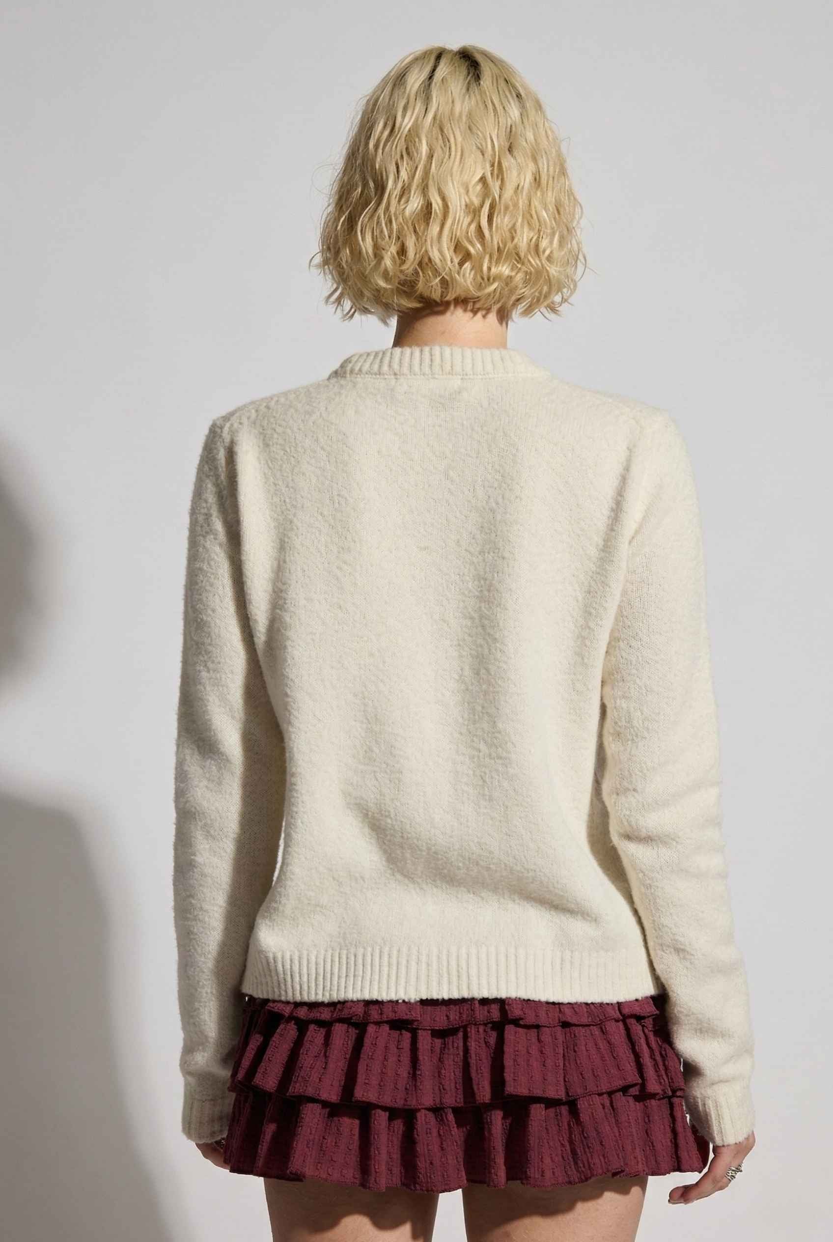 Model wearing Penelope Top in Off White Soft Wool-Blend Crew Neck Button-Up Cardigan with ruffle mini skirt