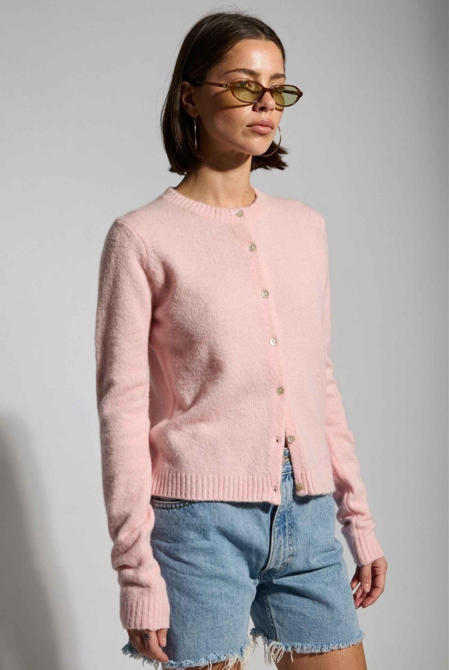 Model wearing Penelope Top in Pink Soft Wool-Blend Crew Neck Button-Up Cardigan with denim shorts 