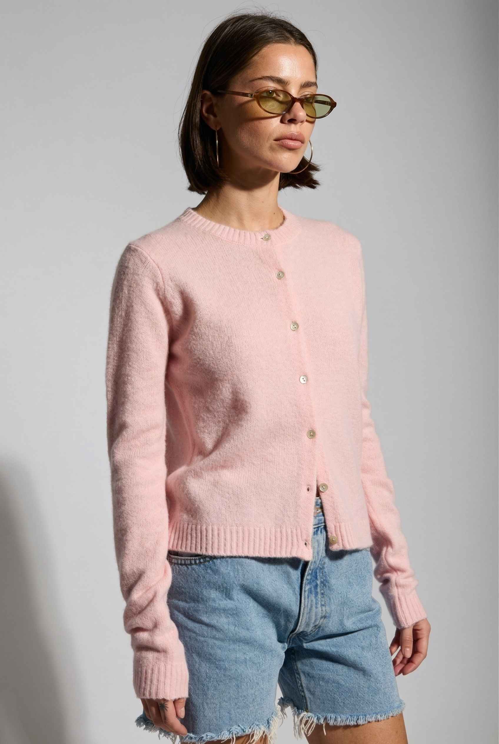 Model wearing Penelope Top in Pink Soft Wool-Blend Crew Neck Button-Up Cardigan with denim shorts 