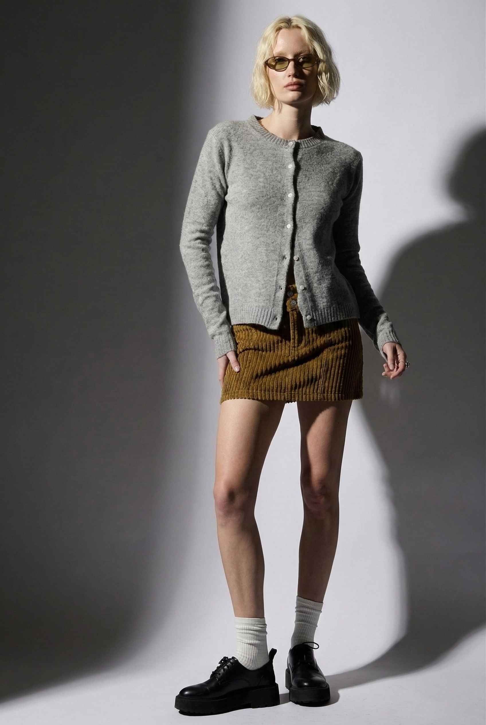 Model wearing Penelope Top in Grey Soft Wool-Blend Crew Neck Button-Up Cardigan with corduroy mini skirt, socks, and loafers 