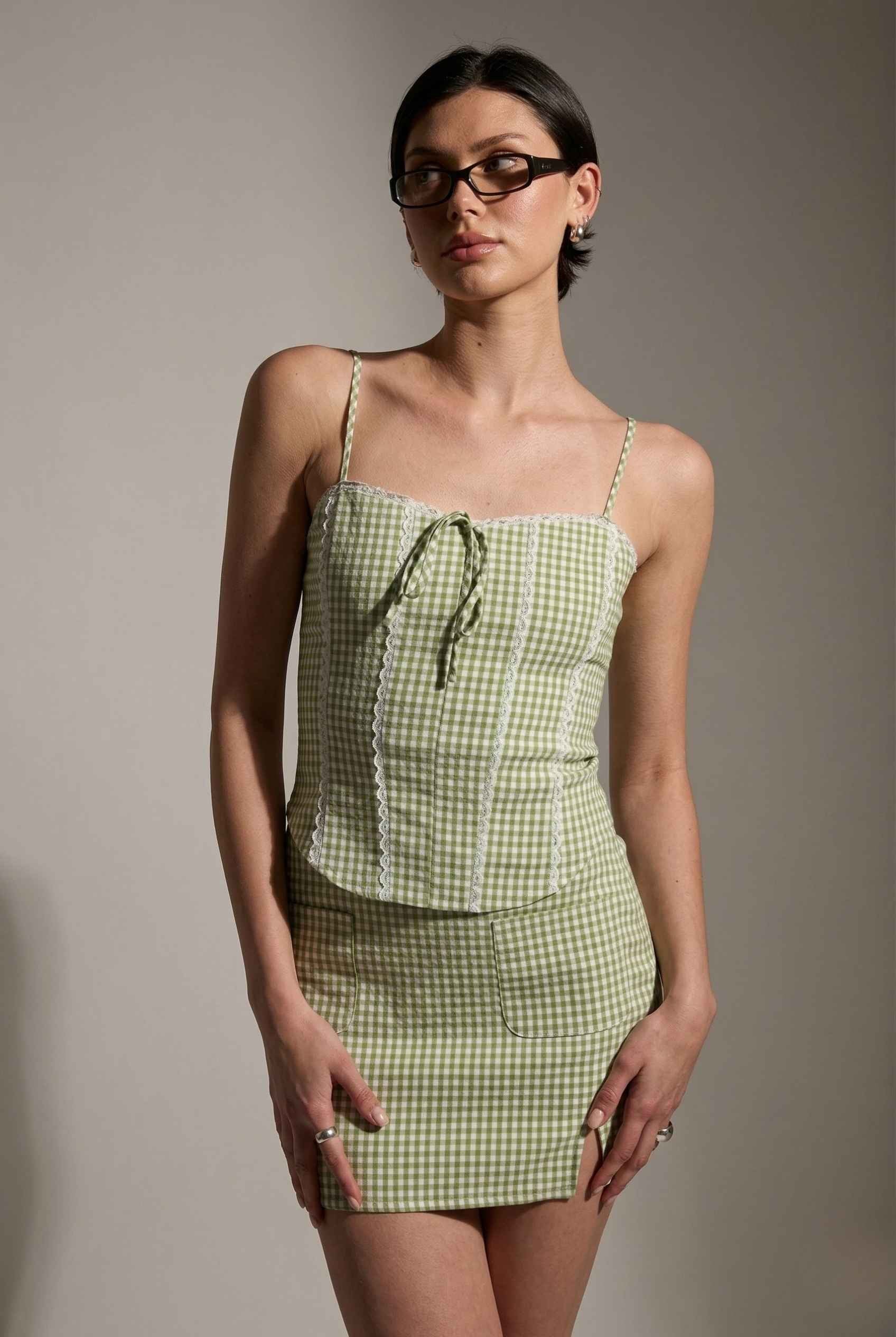 Woman wearing a Piper Top Green Gingham Lace Trim Corset Cami against a plain background