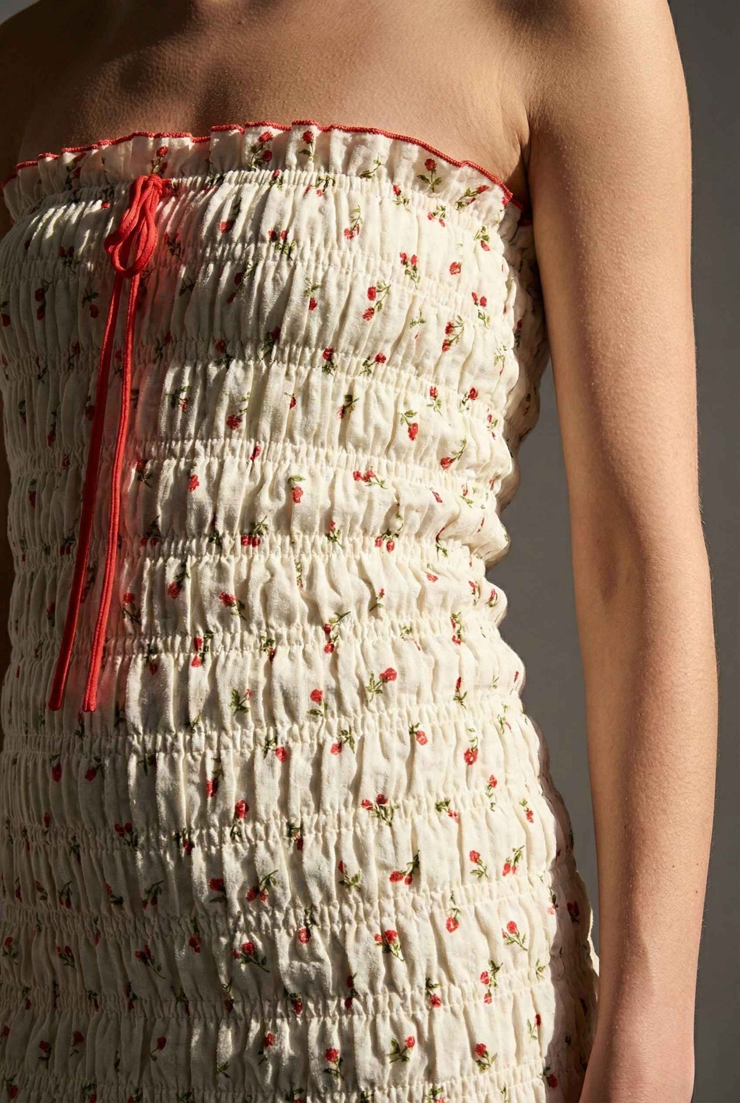 Pippa Mini Cream Smocked Cherry Print Strapless Dress with red floral pattern and red tie detail on a plain background