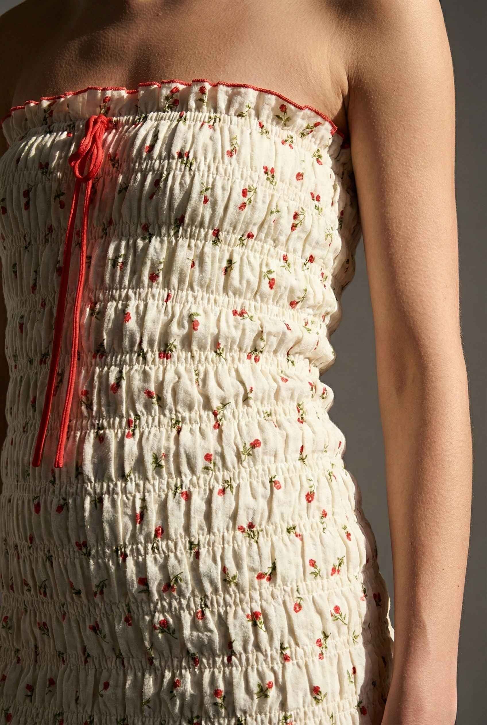 Pippa Mini Cream Smocked Cherry Print Strapless Dress with red floral pattern and red tie detail on a plain background
