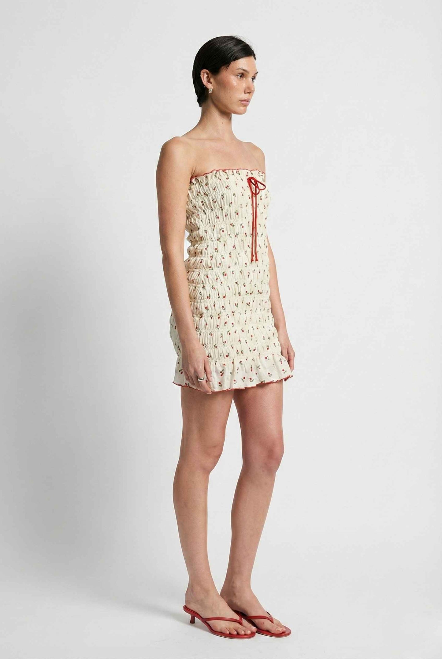 Woman wearing a Pippa Mini Cream Smocked Cherry Print Strapless Dress on a white background