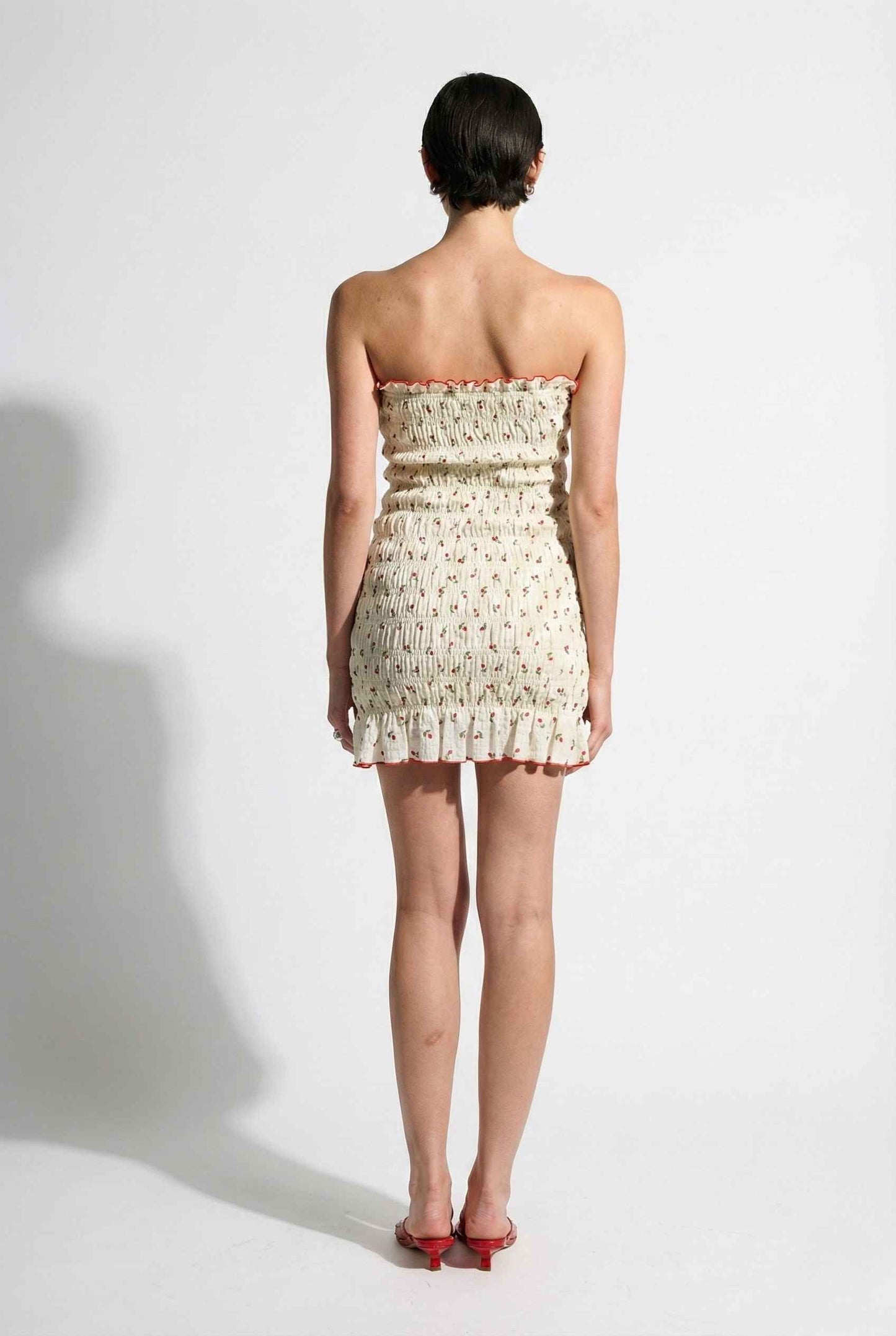 Woman wearing a Pippa Mini Cream Smocked Cherry Print Strapless Dress on a white background