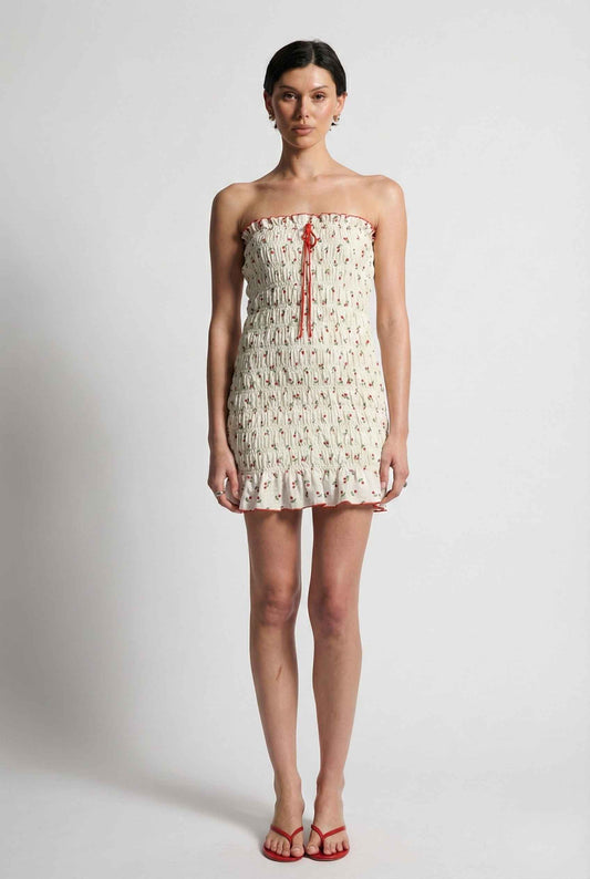 Woman wearing a Pippa Mini Cream Smocked Cherry Print Strapless Dress on a plain background
