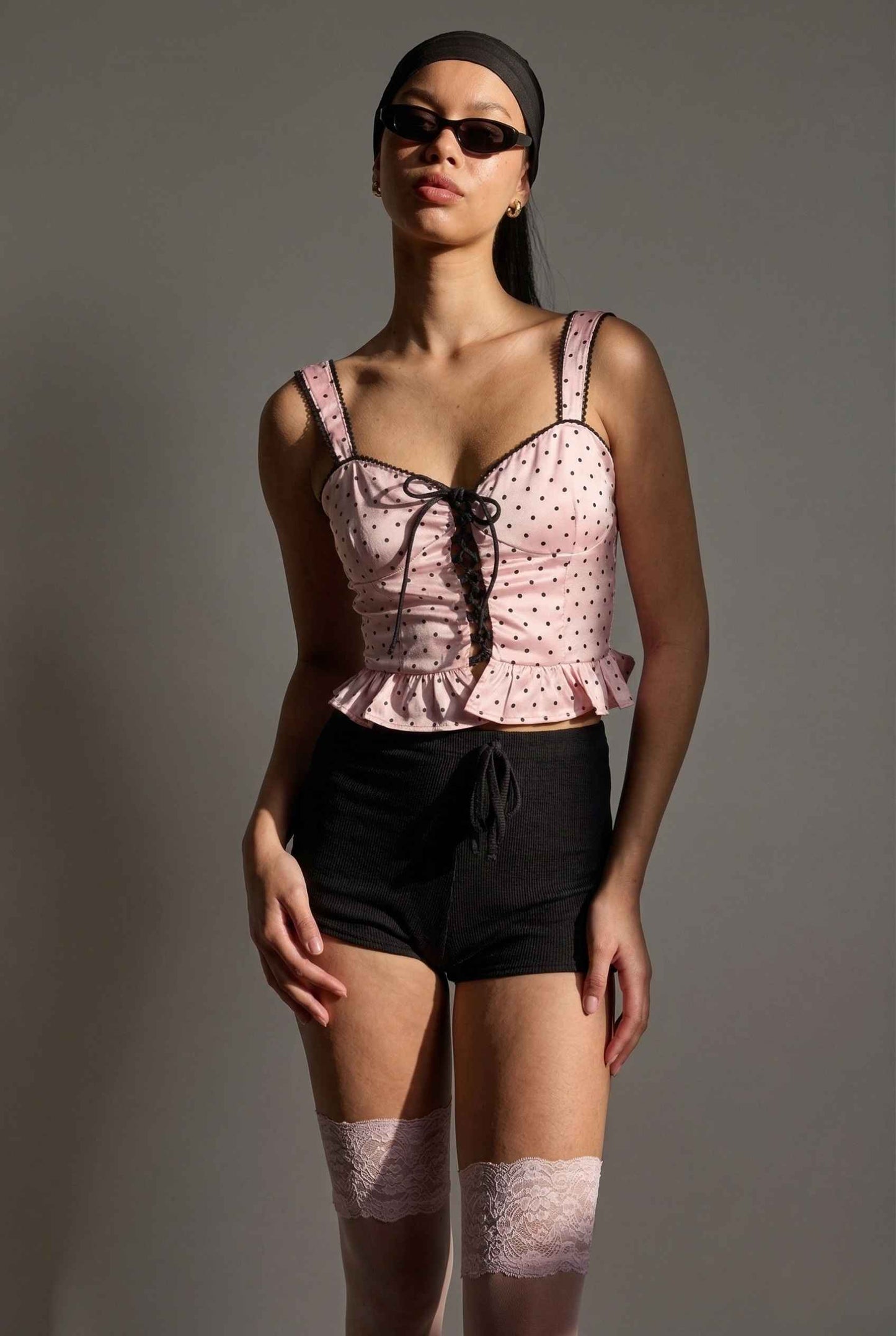 Woman wearing a Pippa Top Pink & Black Polka Dot Lace Trim Corset and black shorts with a gray background