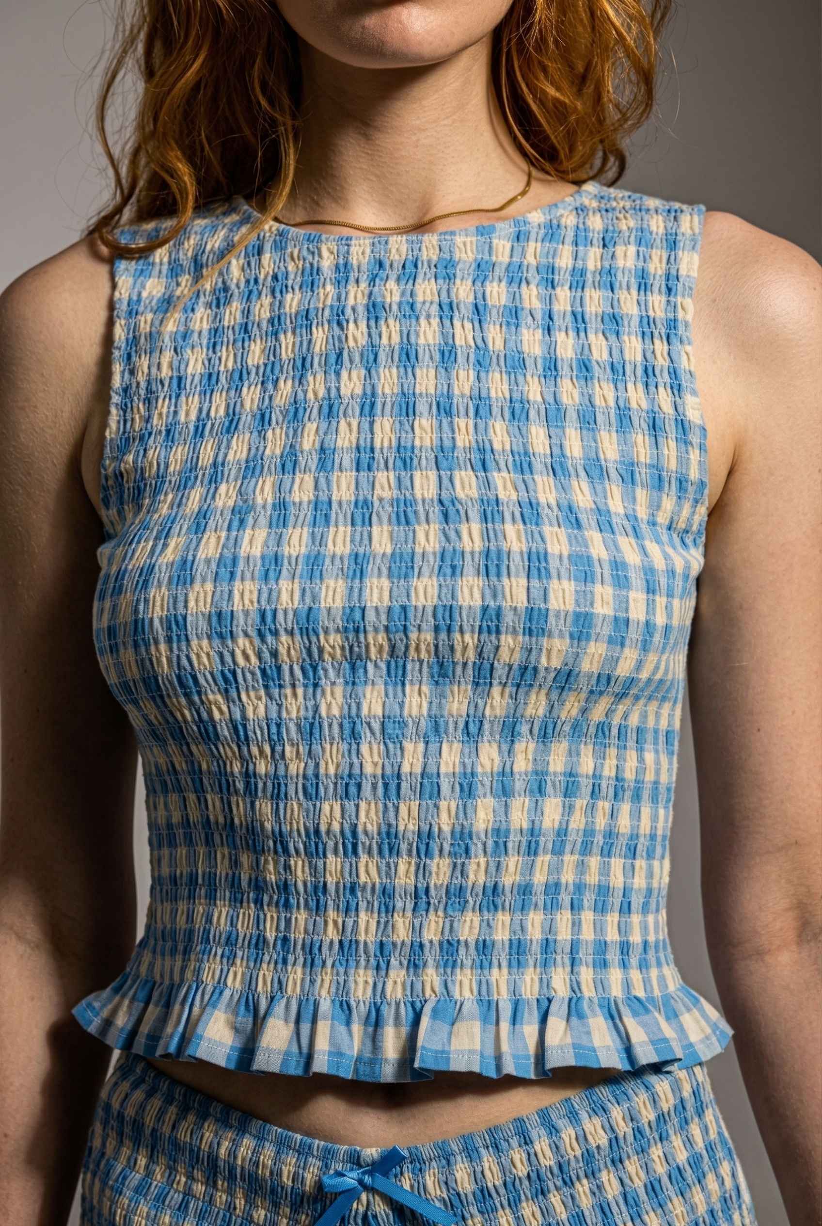 Person wearing a Poppy Top Blue Gingham Smocked Sleeveless Knit with ruffled details.