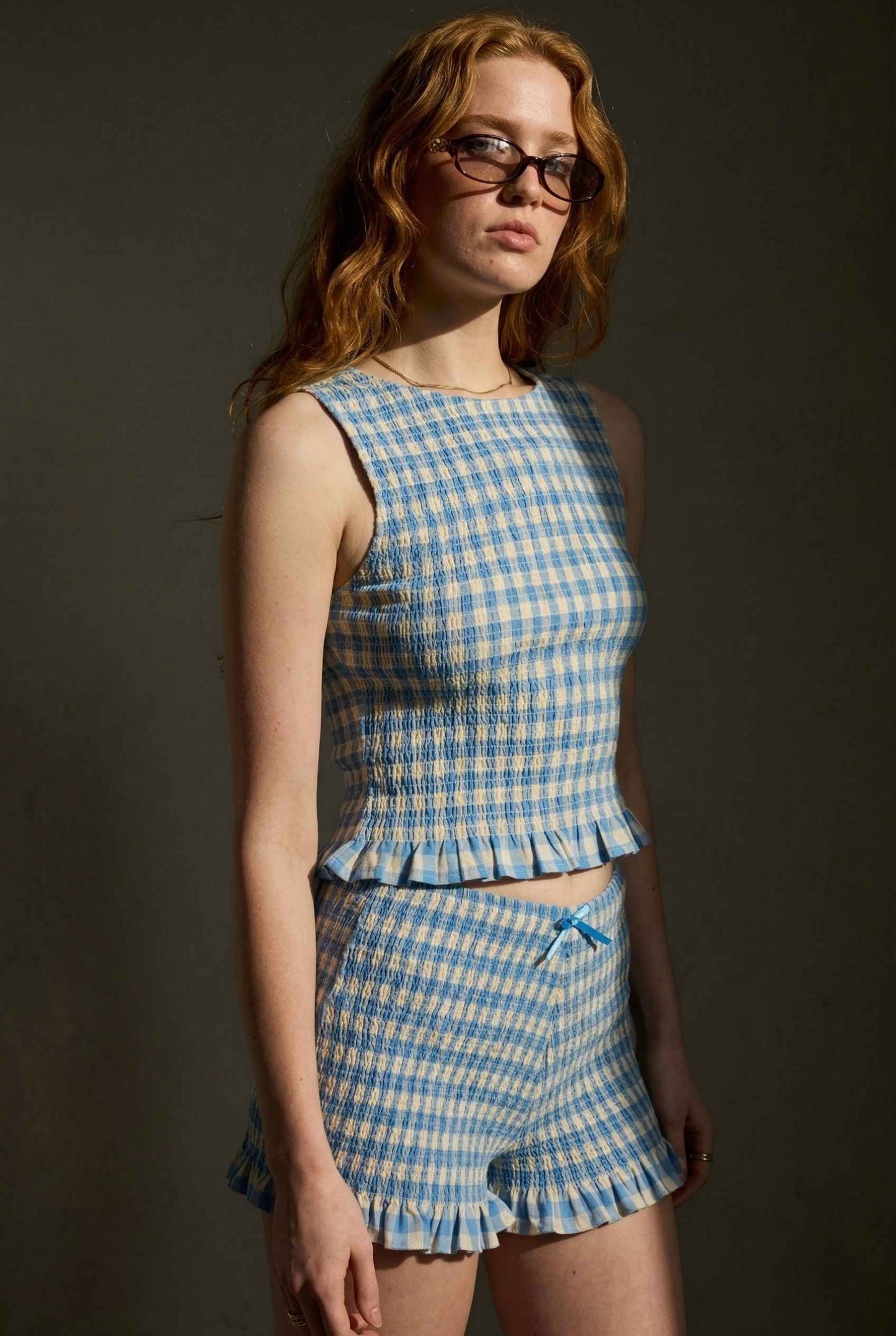 Woman wearing a Poppy Top Blue Gingham Smocked Sleeveless Knit against a dark background