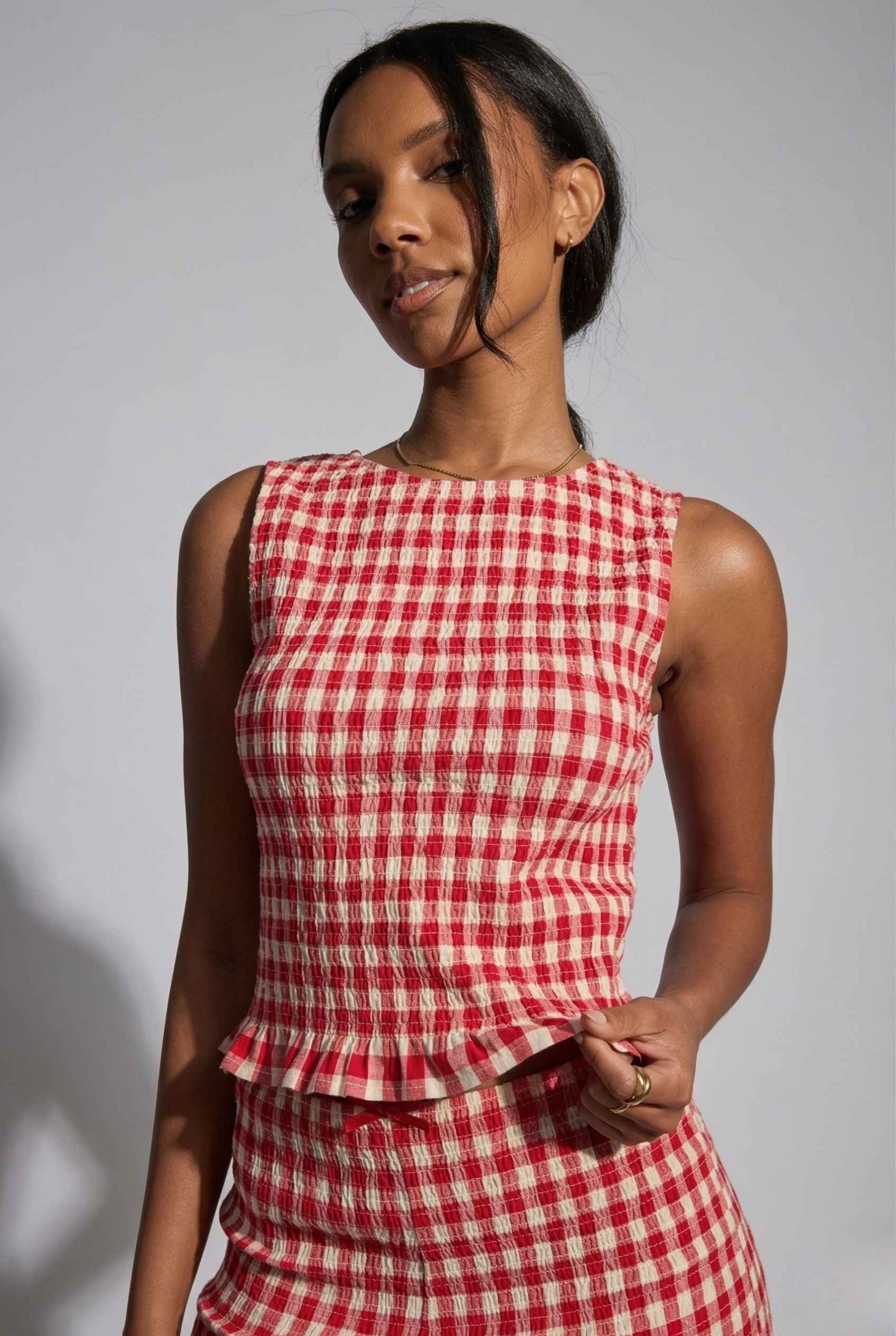 Woman wearing a Poppy Top Red Gingham Smocked Sleeveless Knit against a gray background