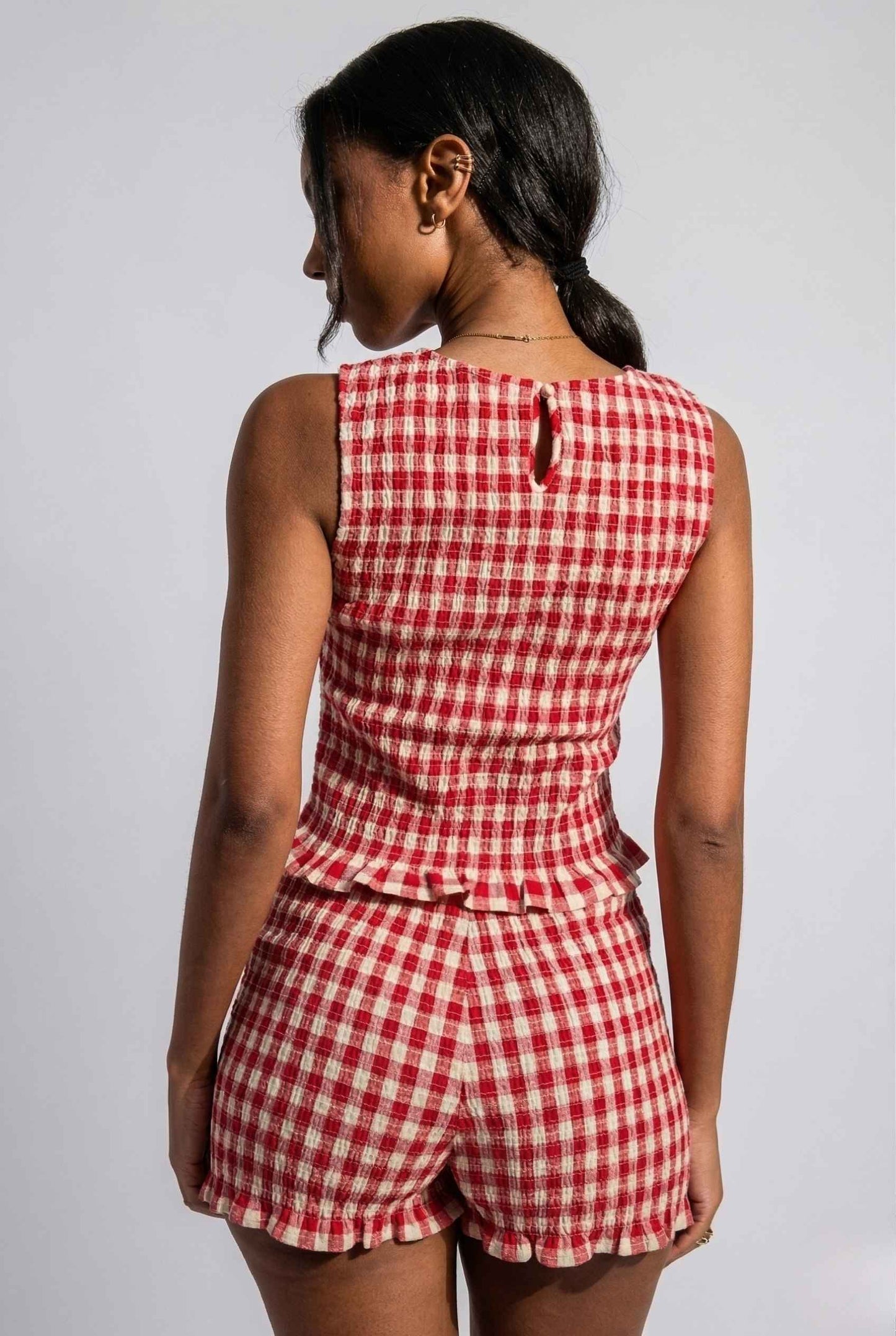 Woman wearing a rPoppy Top Red Gingham Smocked Sleeveless Knit against a plain background