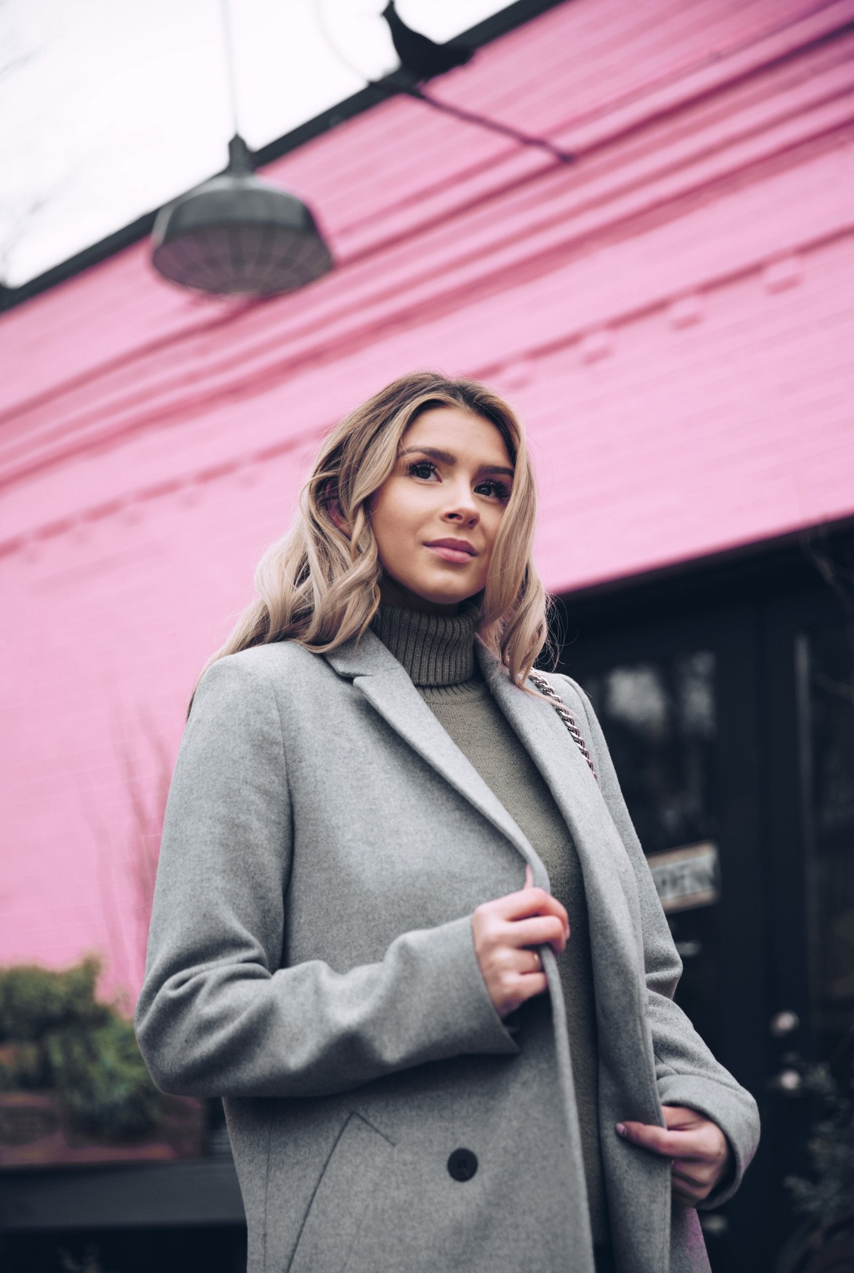 Woman in a gray coat standing in front of a pink building