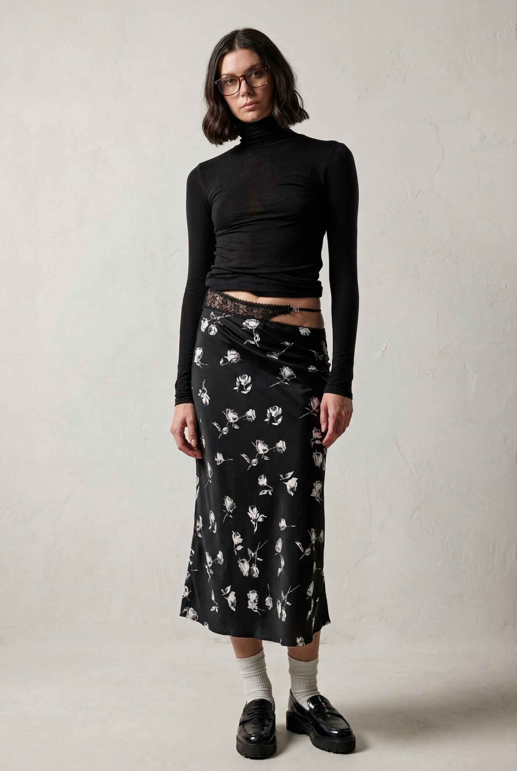 Model wearing Raven Skirt in Black Floral Satin Midi Skirt with Lace Waist paired with basic turtle neck and shiny loafers with tall socks