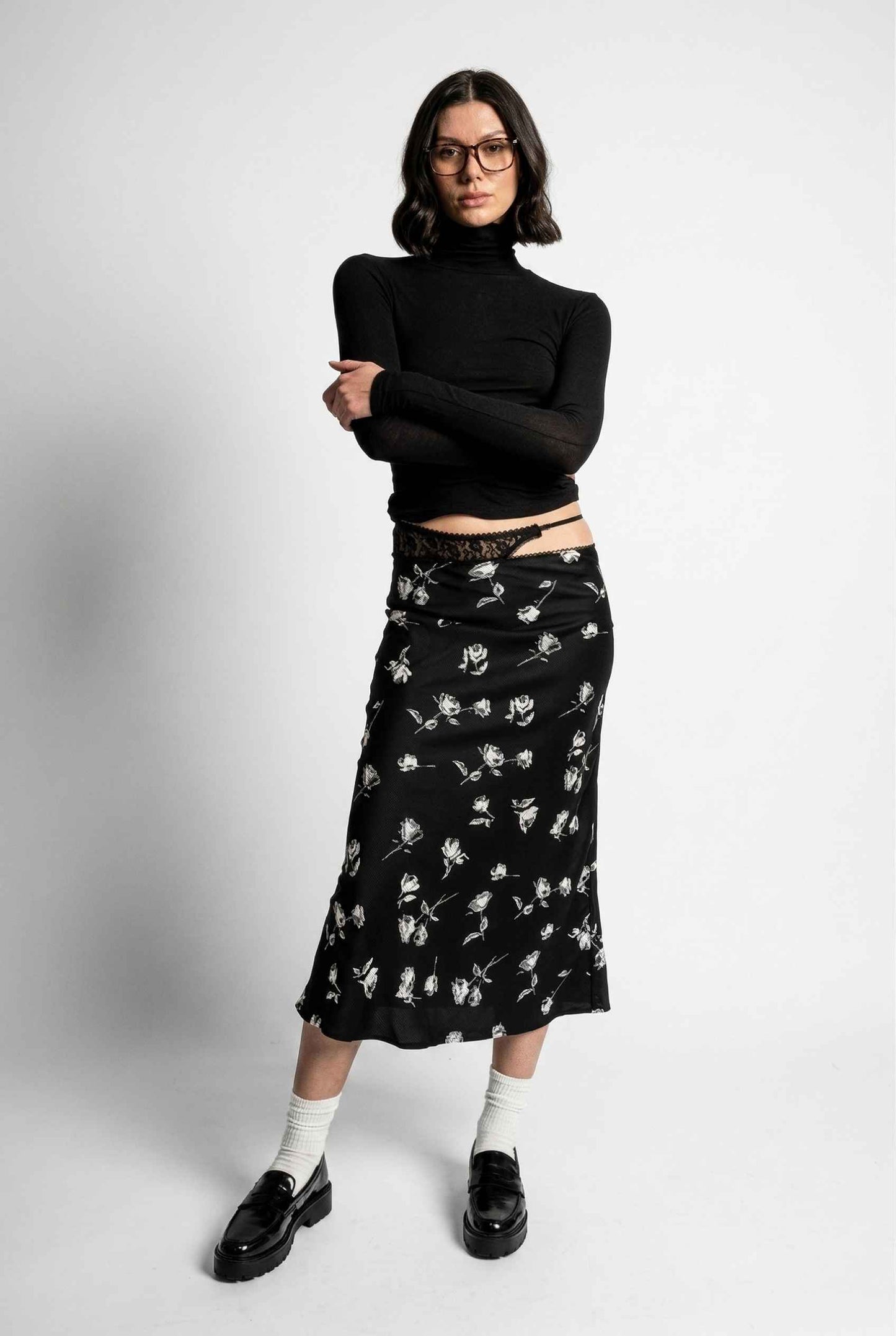 Model wearing Raven Skirt in Black Floral Satin Midi Skirt with Lace Waist paired with basic turtle neck and shiny loafers with tall socks
