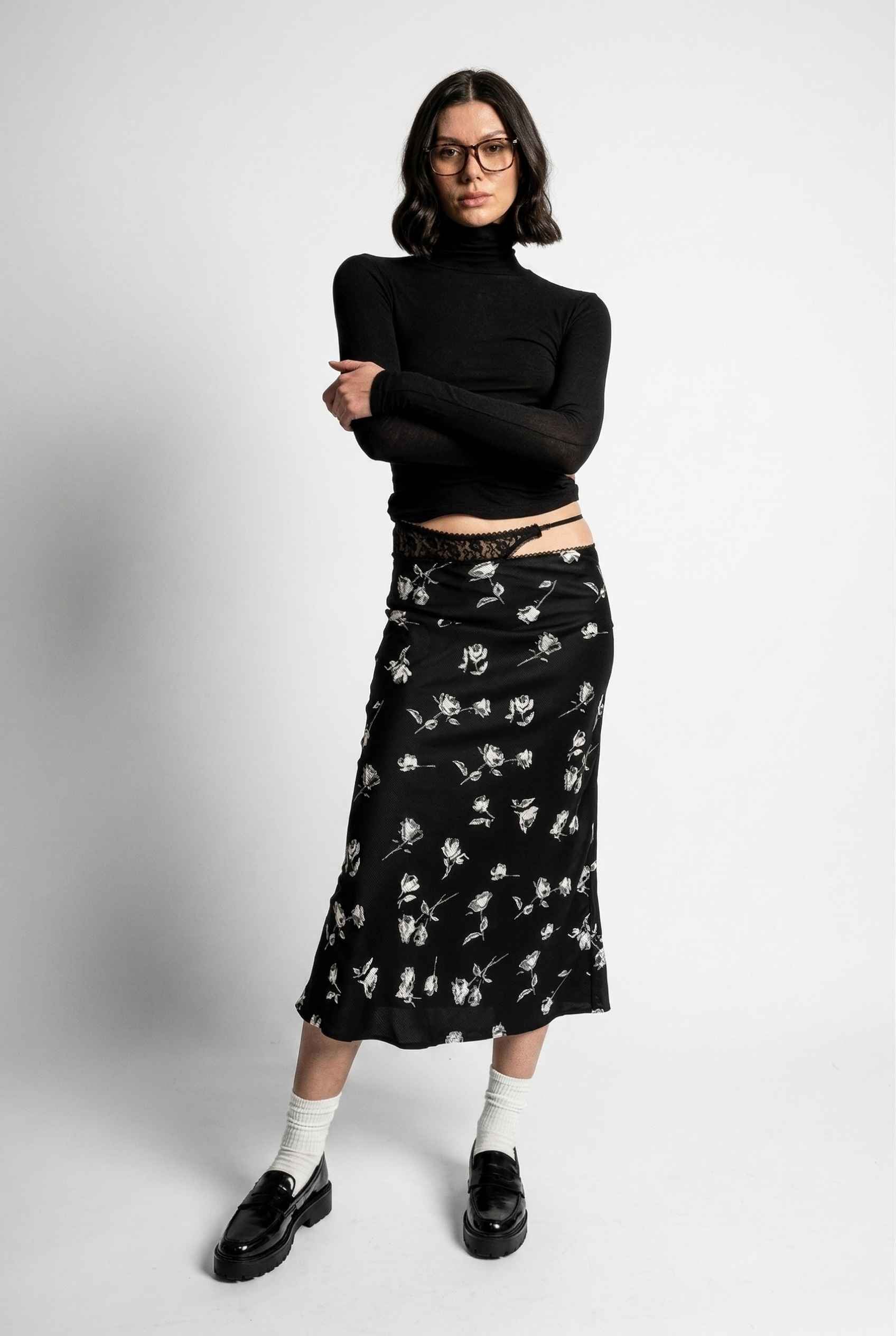 Model wearing Raven Skirt in Black Floral Satin Midi Skirt with Lace Waist paired with basic turtle neck and shiny loafers with tall socks