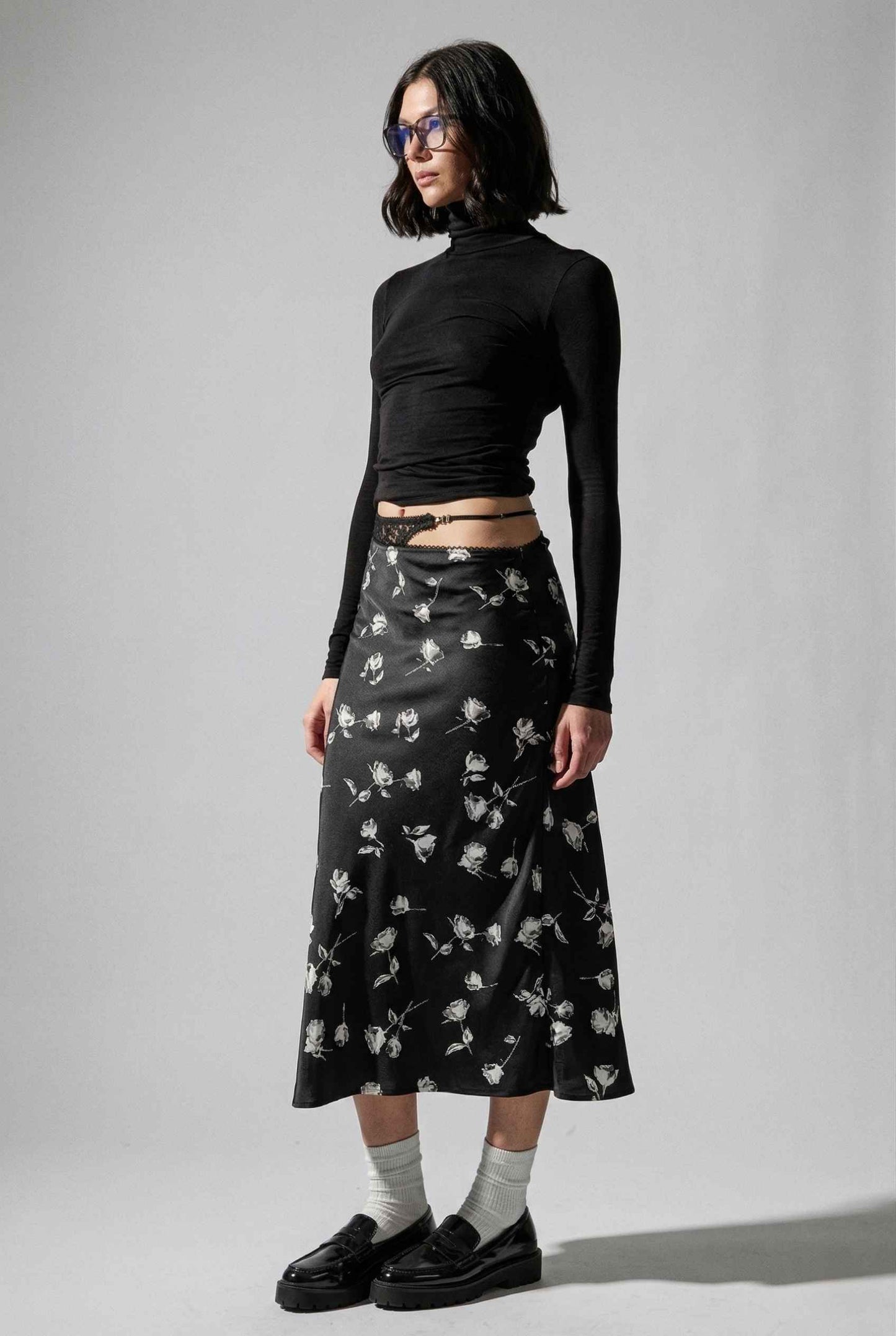 Model wearing Raven Skirt in Black Floral Satin Midi Skirt with Lace Waist paired with basic turtle neck and shiny loafers with tall socks