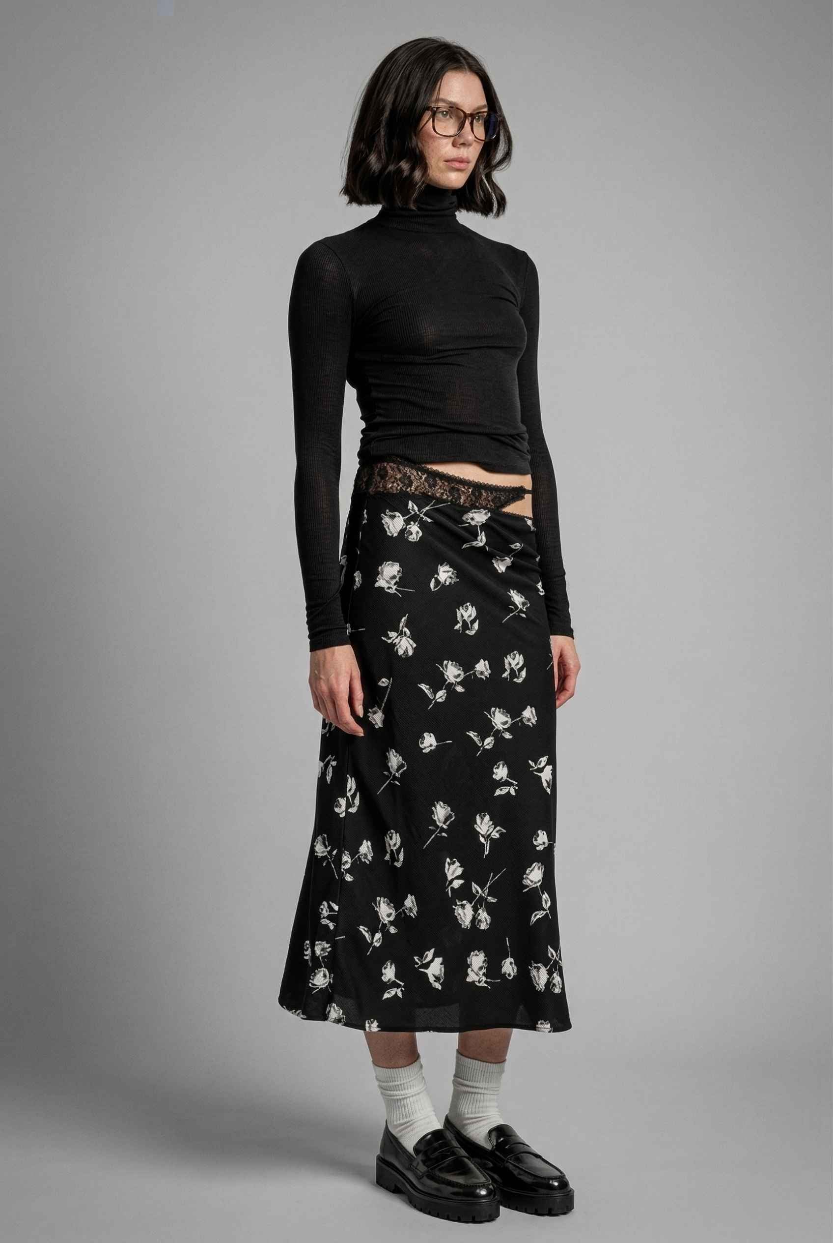 Model wearing Raven Skirt in Black Floral Satin Midi Skirt with Lace Waist paired with basic turtle neck and shiny loafers with tall socks