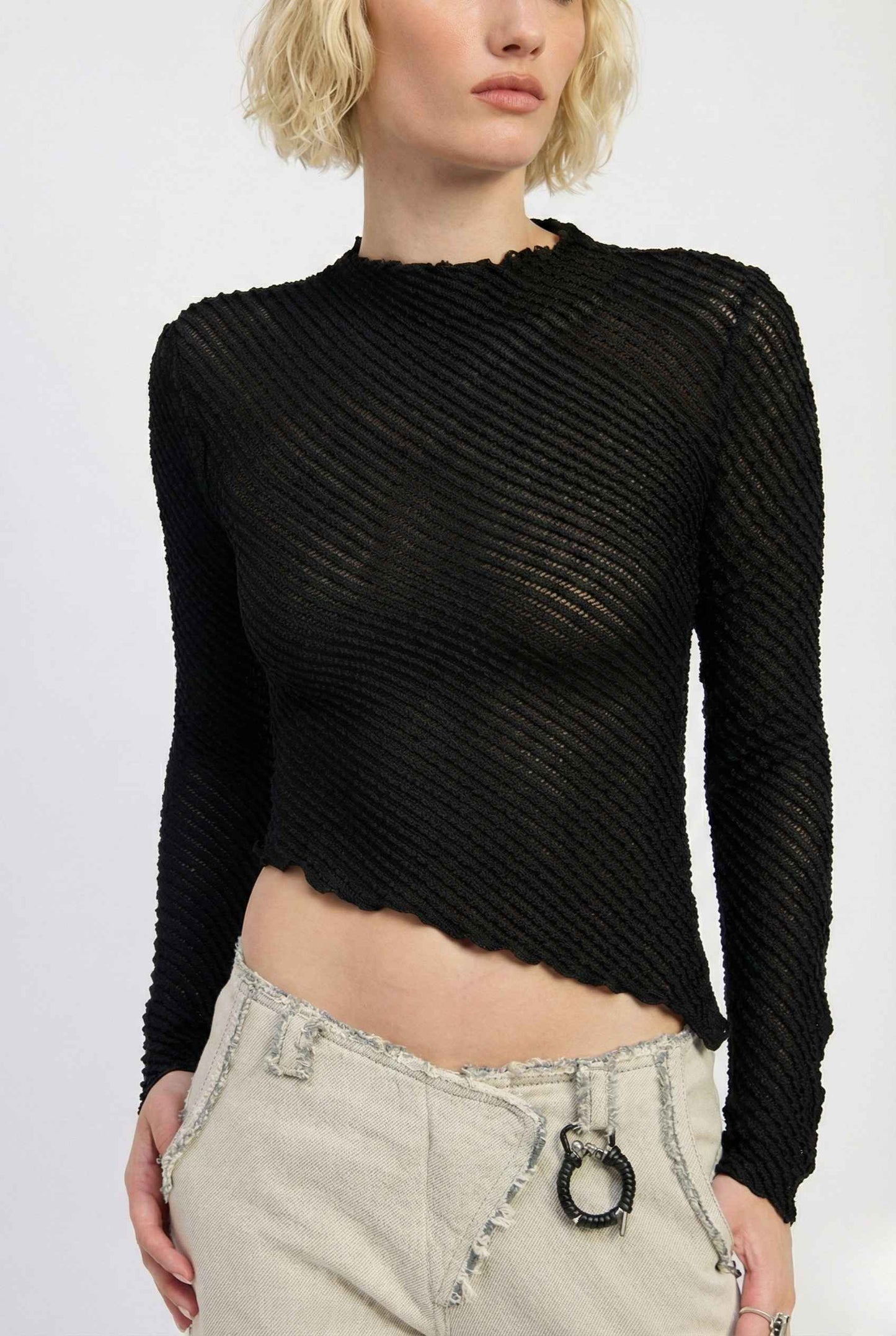 Woman wearing a Ren Top Black Asymmetrical Diagonal Rib Long Sleeve and light-colored pants on a white background