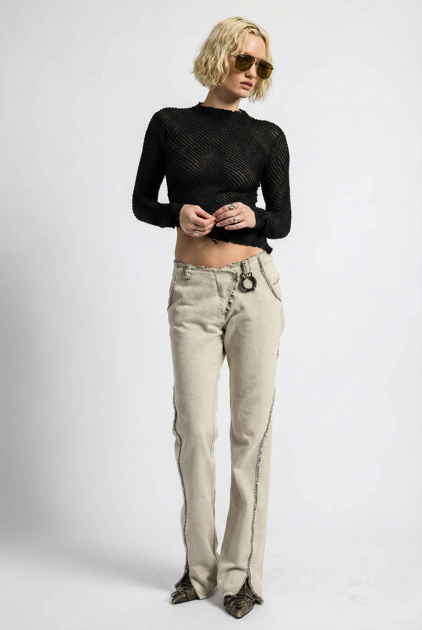 Person wearing a Ren Top Black Asymmetrical Diagonal Rib Long Sleeve and beige flared jeans on a white background