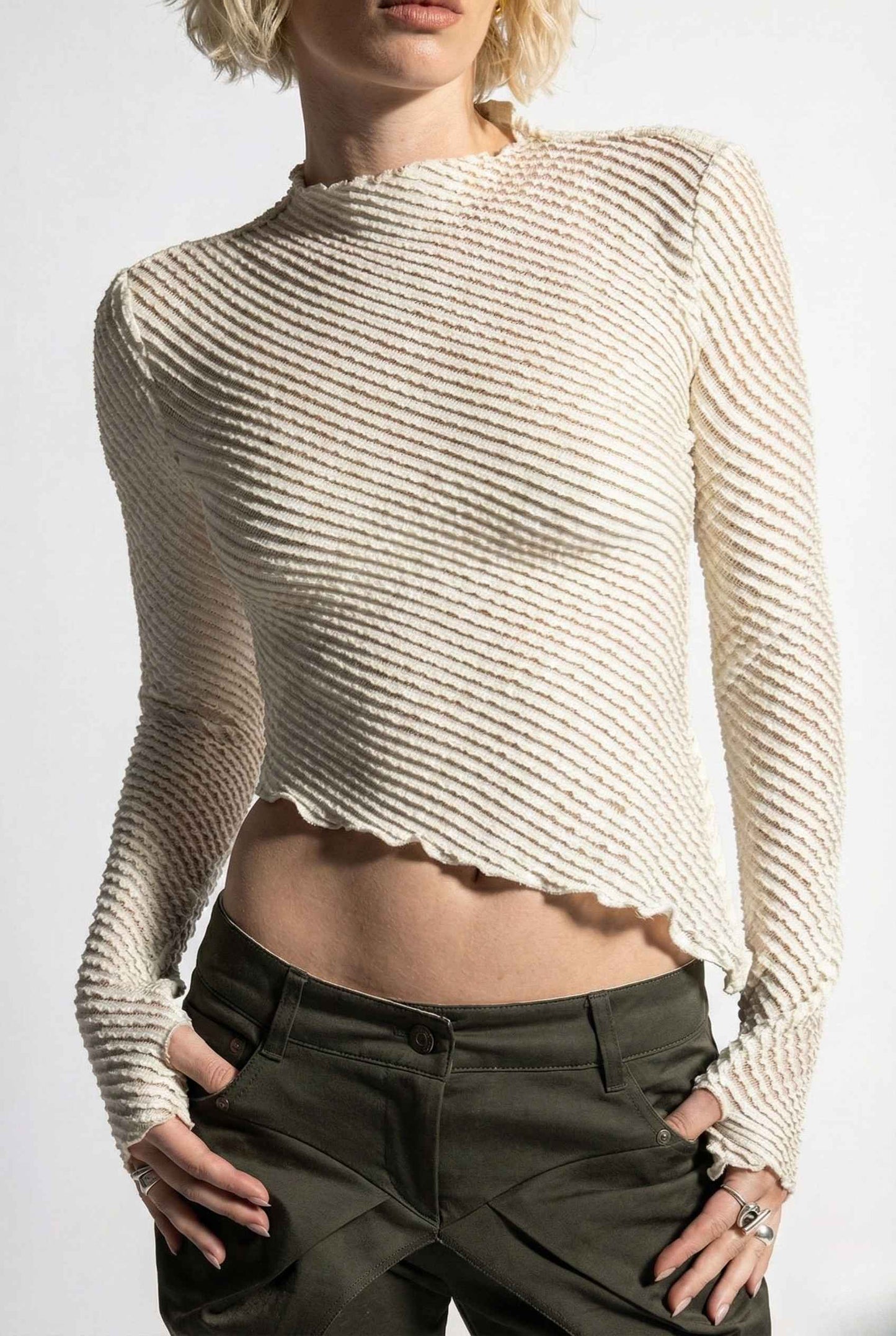 Person wearing a Ren Top Cream Asymmetrical Diagonal Rib Long Sleeve and dark pants on a plain background