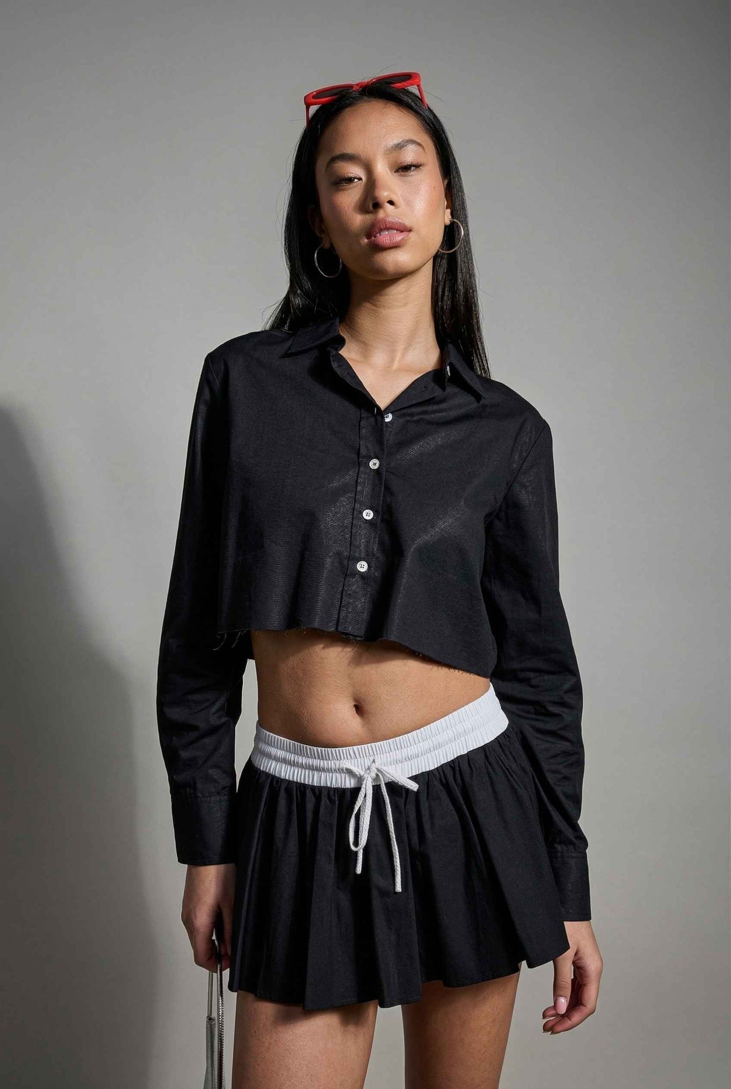Model wearing Riley Skirt in Black Cotton Poplin Boxer Waist Mini Skirt paired with matching poplin long sleeve button top 