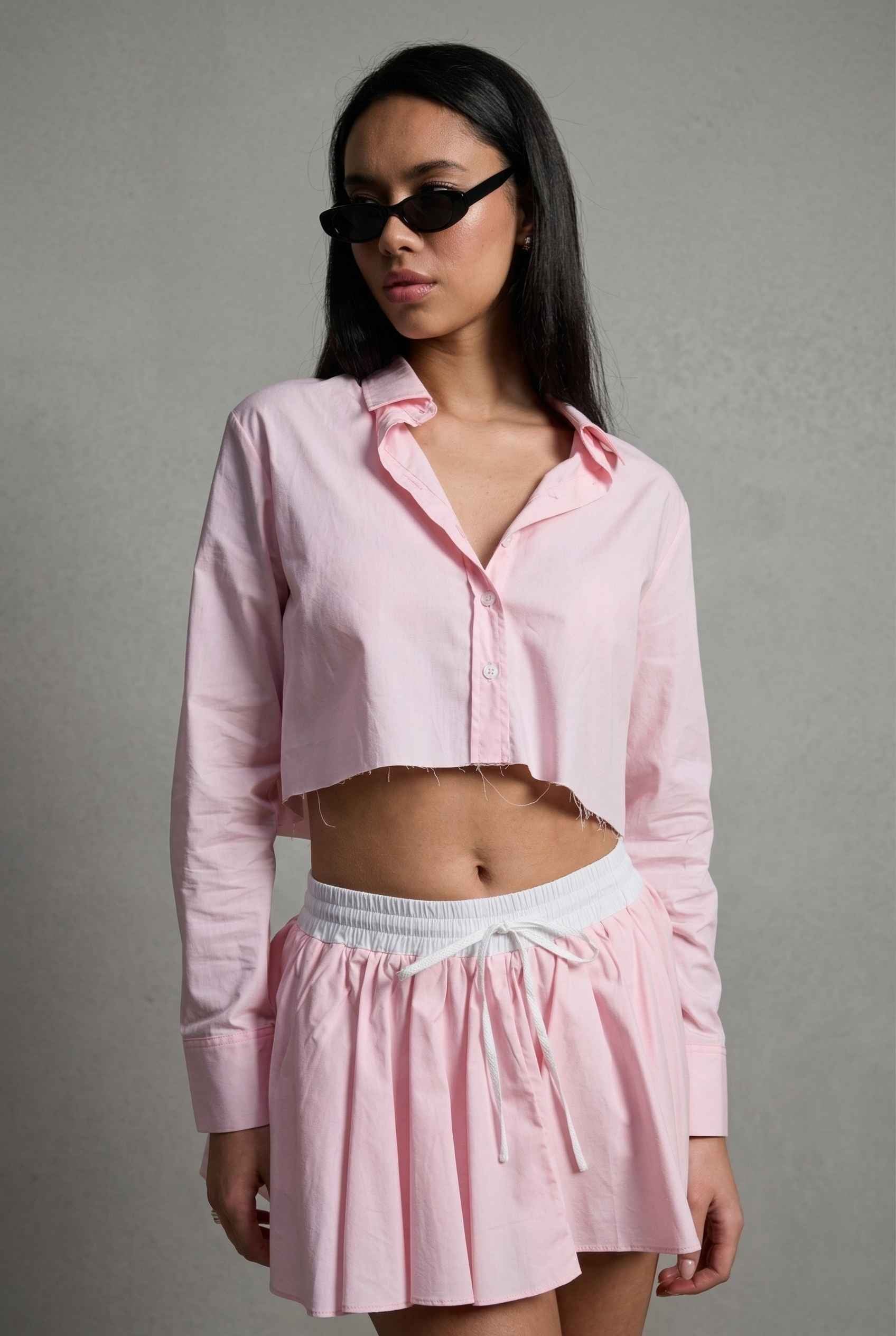 Model wearing Riley Skirt in Pink Cotton Poplin Boxer Waist Mini Skirt paired with matching poplin long sleeve button top