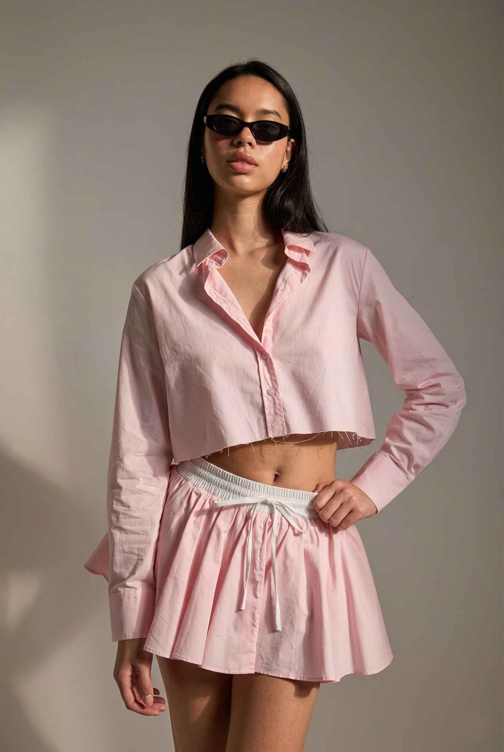 Model wearing Riley Skirt in Pink Cotton Poplin Boxer Waist Mini Skirt paired with matching poplin long sleeve button top