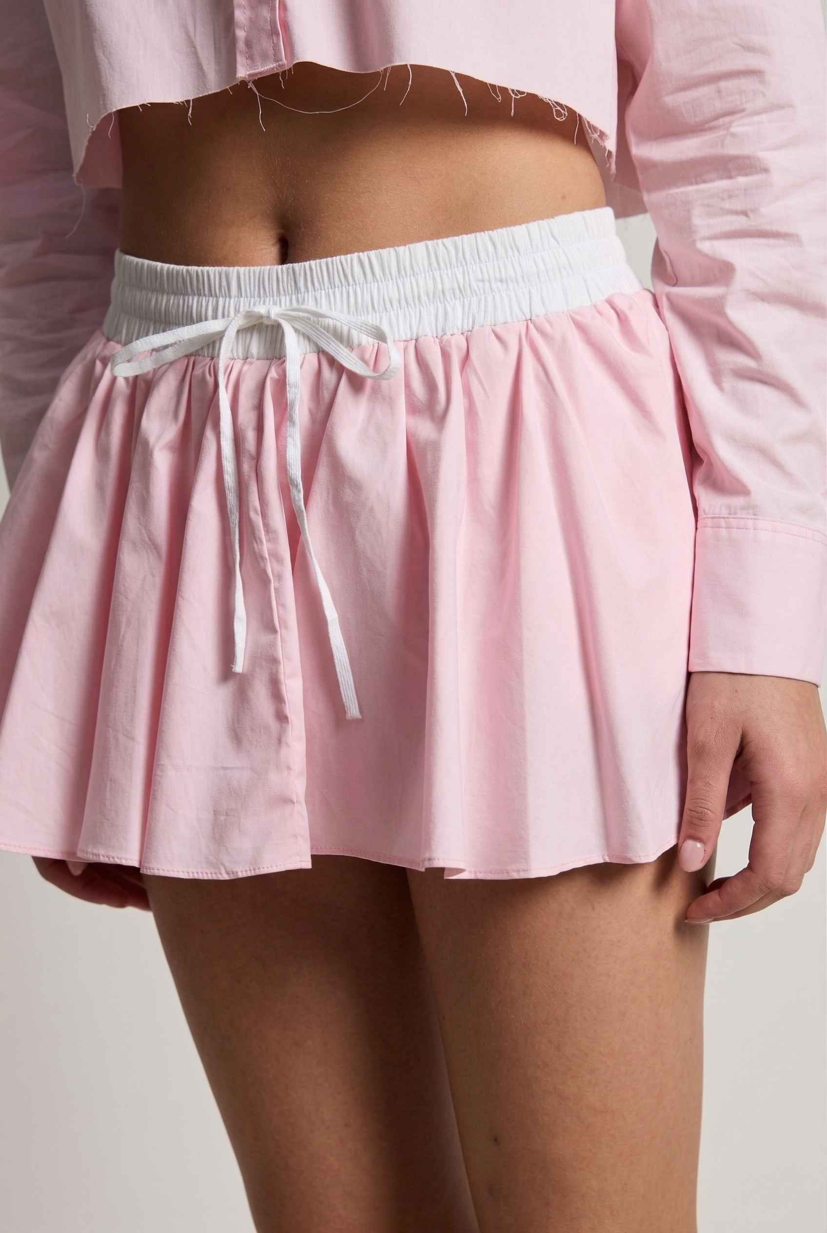 Model wearing Riley Skirt in Pink Cotton Poplin Boxer Waist Mini Skirt paired with matching poplin long sleeve button top close up tied detail