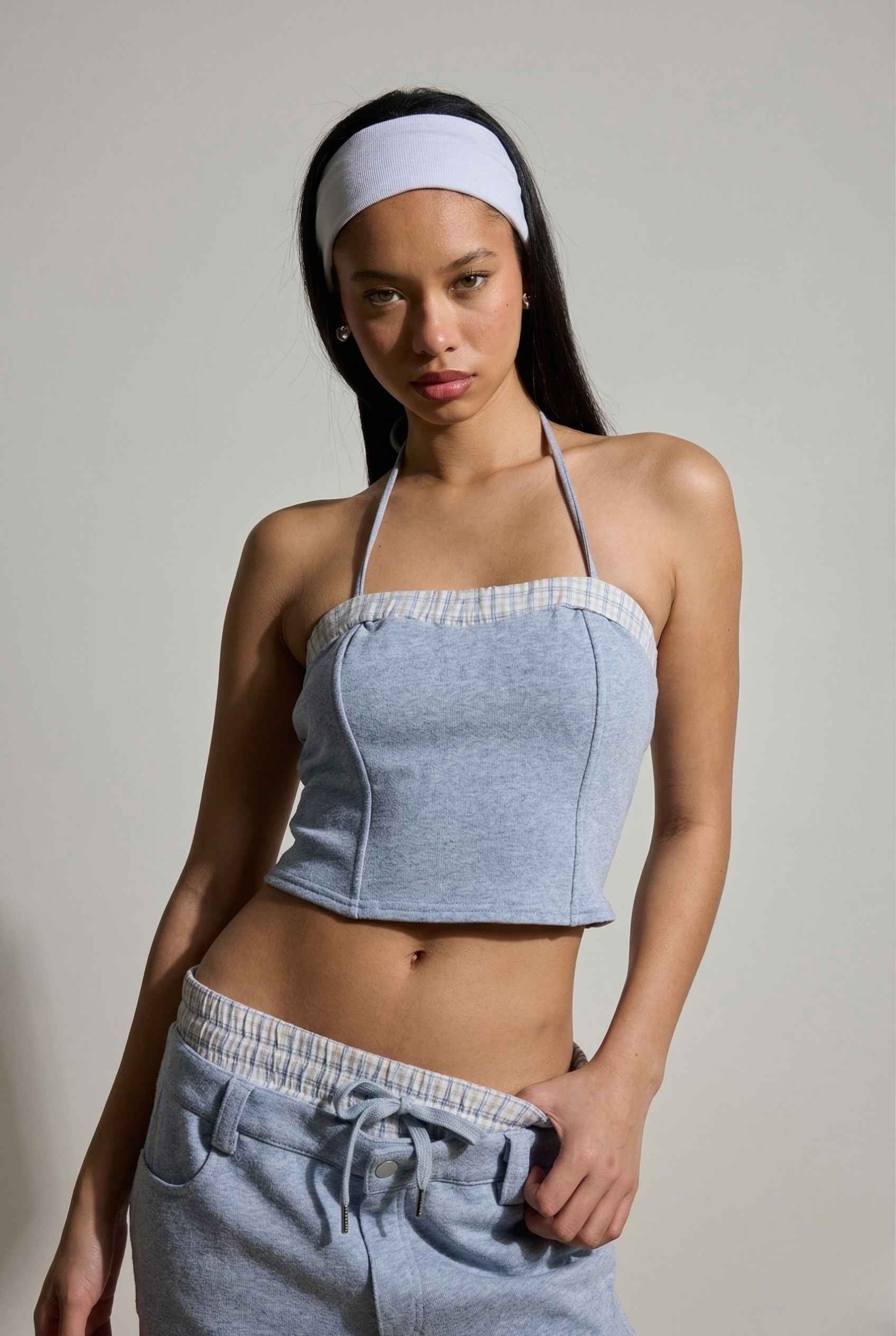 Woman wearing a Riley Top Light Blue Heathered Halter with Plaid Trim and gray sweatpants against a plain background