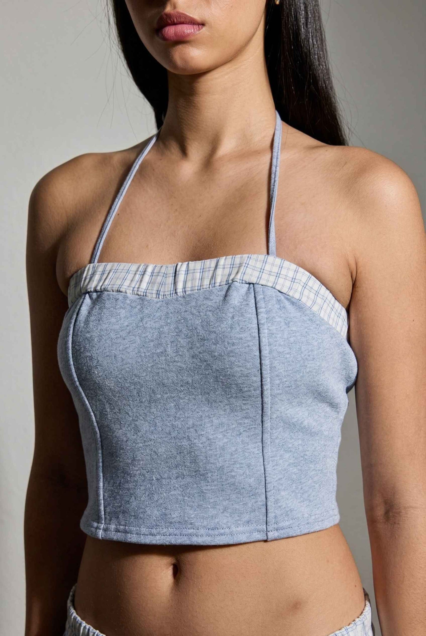Woman wearing a lRiley Top Light Blue Heathered Halter with Plaid Trim against a neutral background