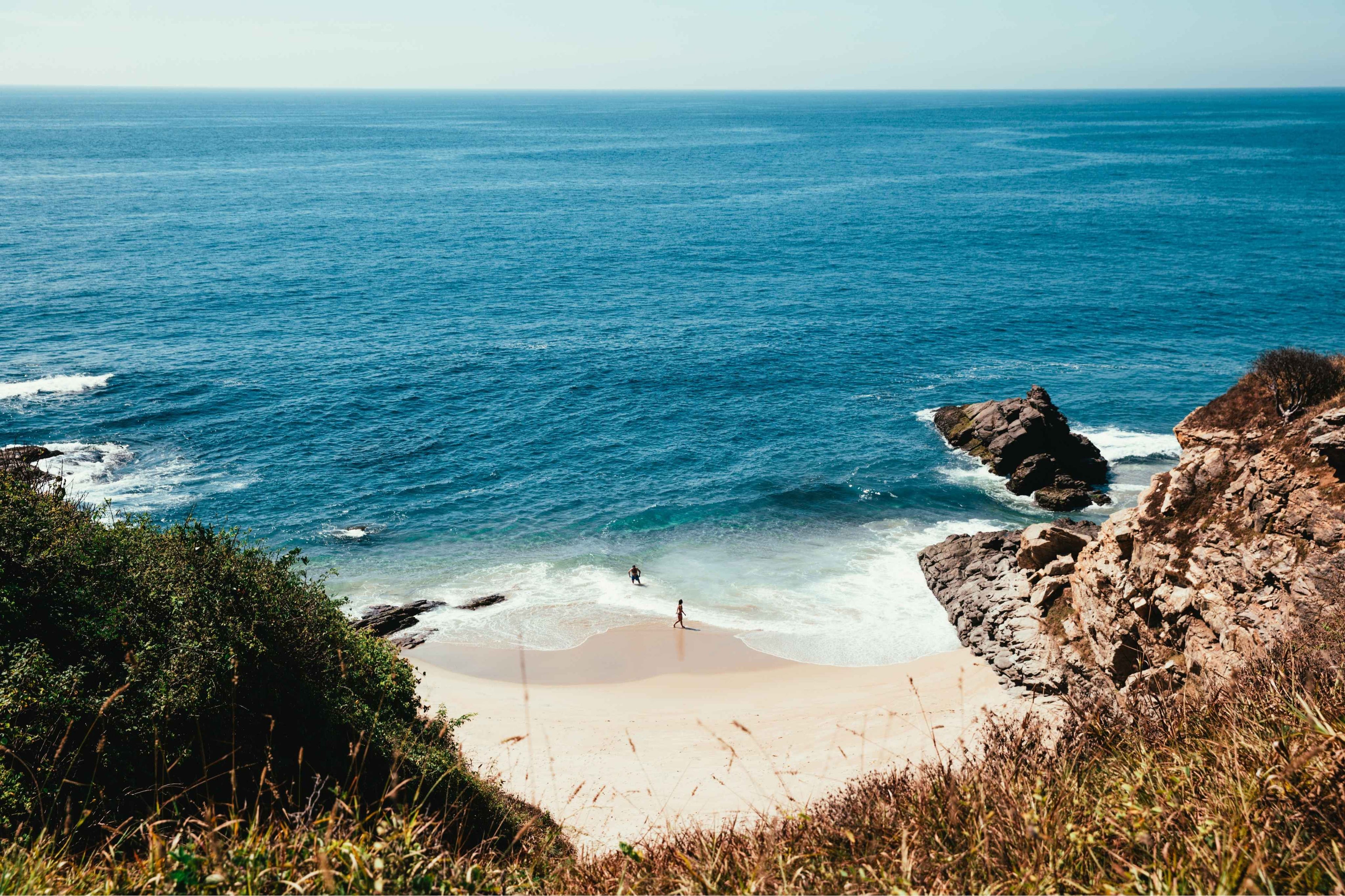 Beach with people on a sandbar surrounded by blue ocean and cliffs.