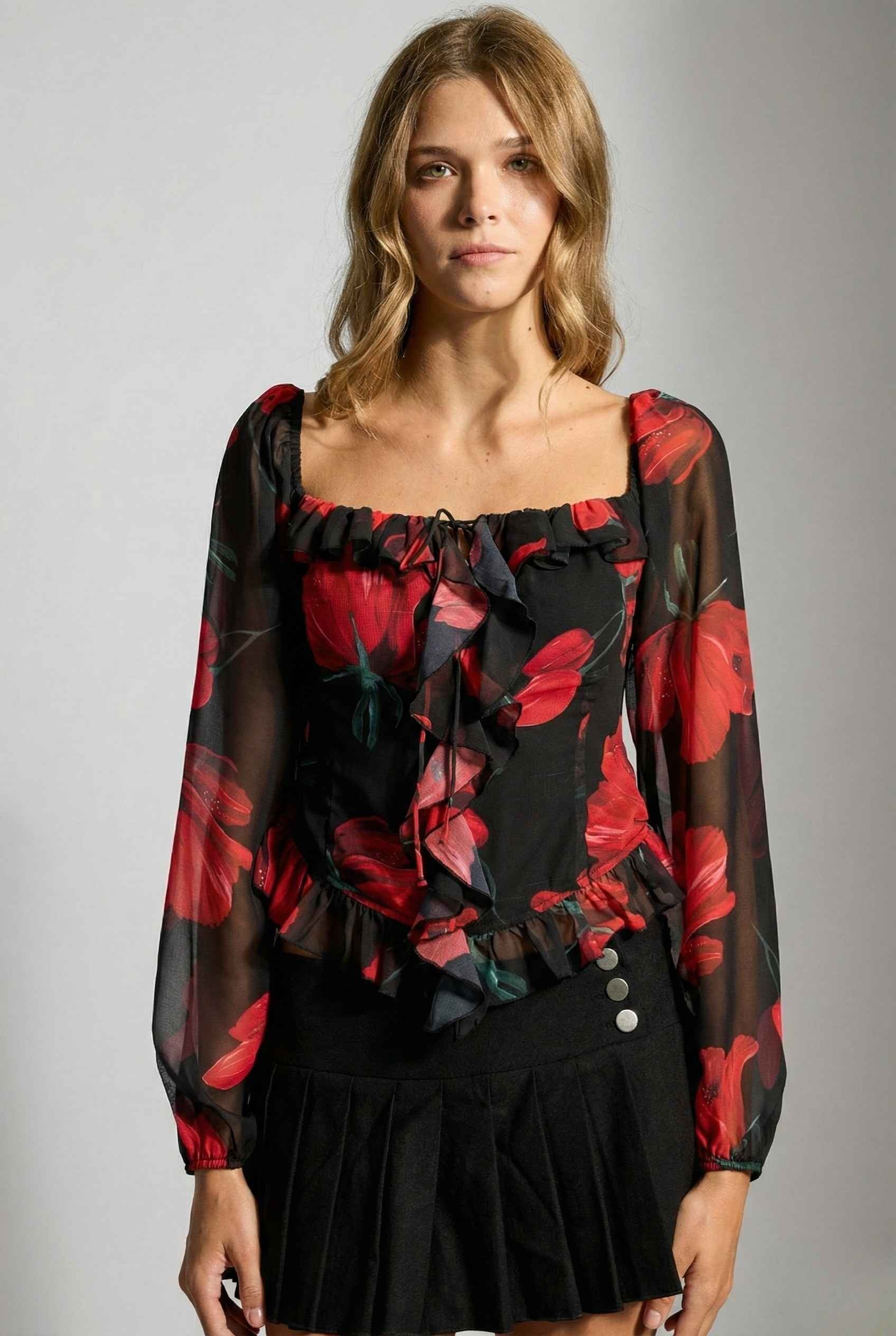 Woman wearing a Rosalia Blouse Black & Red Rose Print Ruffle Top with red floral pattern against a gray background