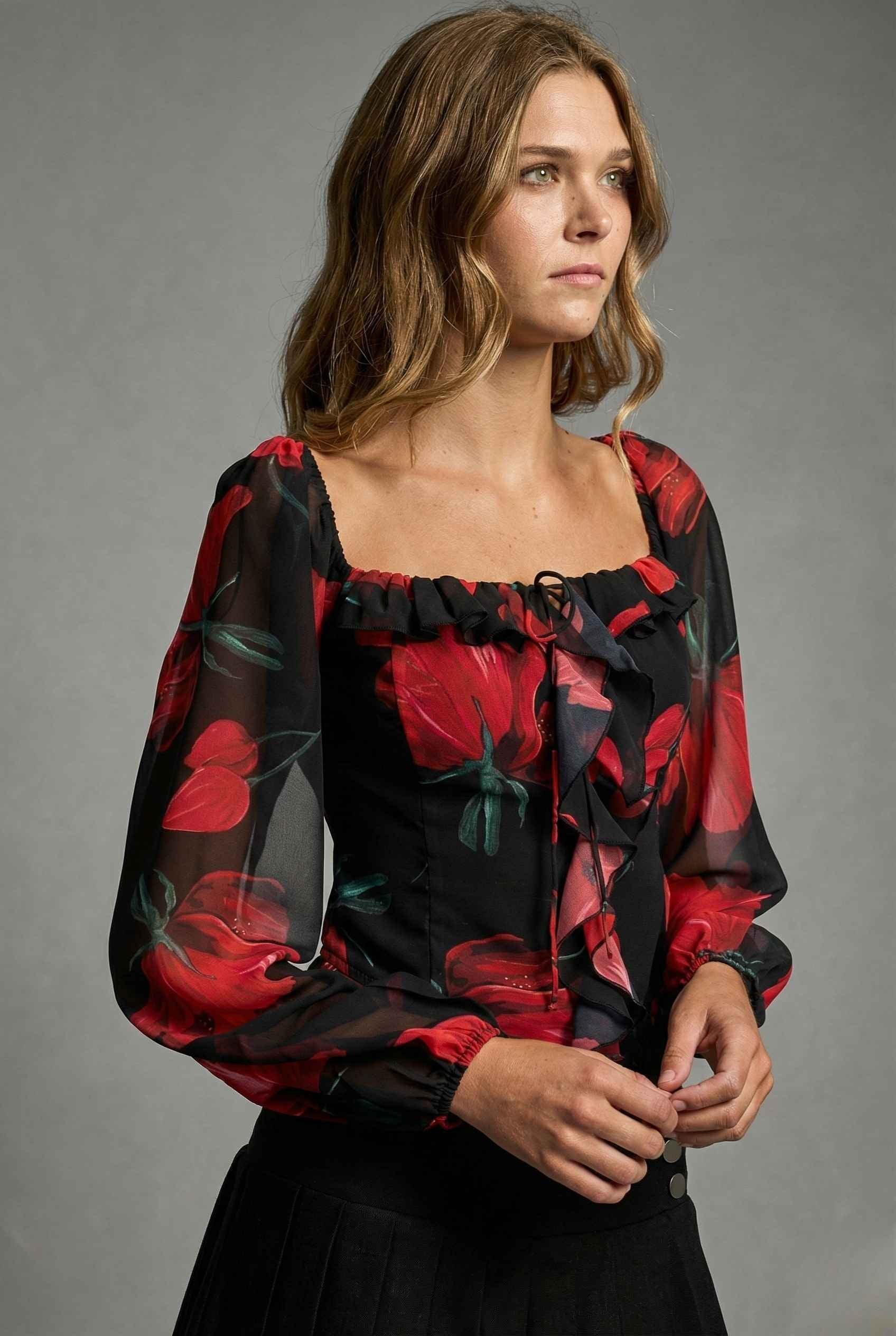 Woman wearing a Rosalia Blouse Black & Red Rose Print Ruffle Top with red floral patterns on a gray background