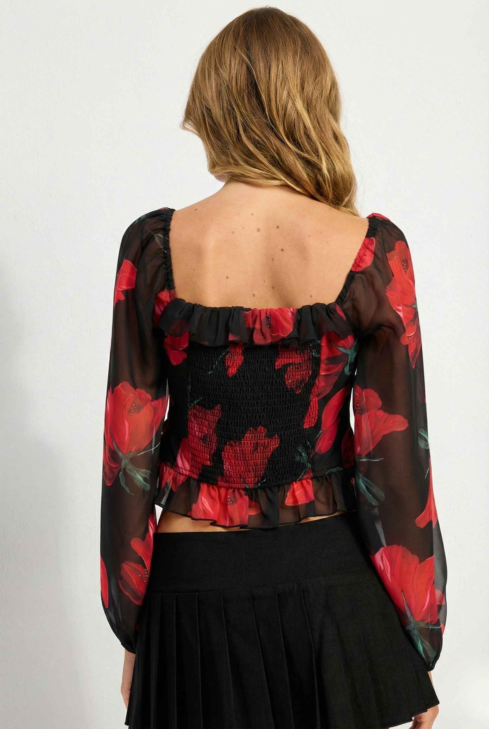 Rosalia Blouse Black & Red Rose Print Ruffle Top with red floral pattern worn by a person on a white background