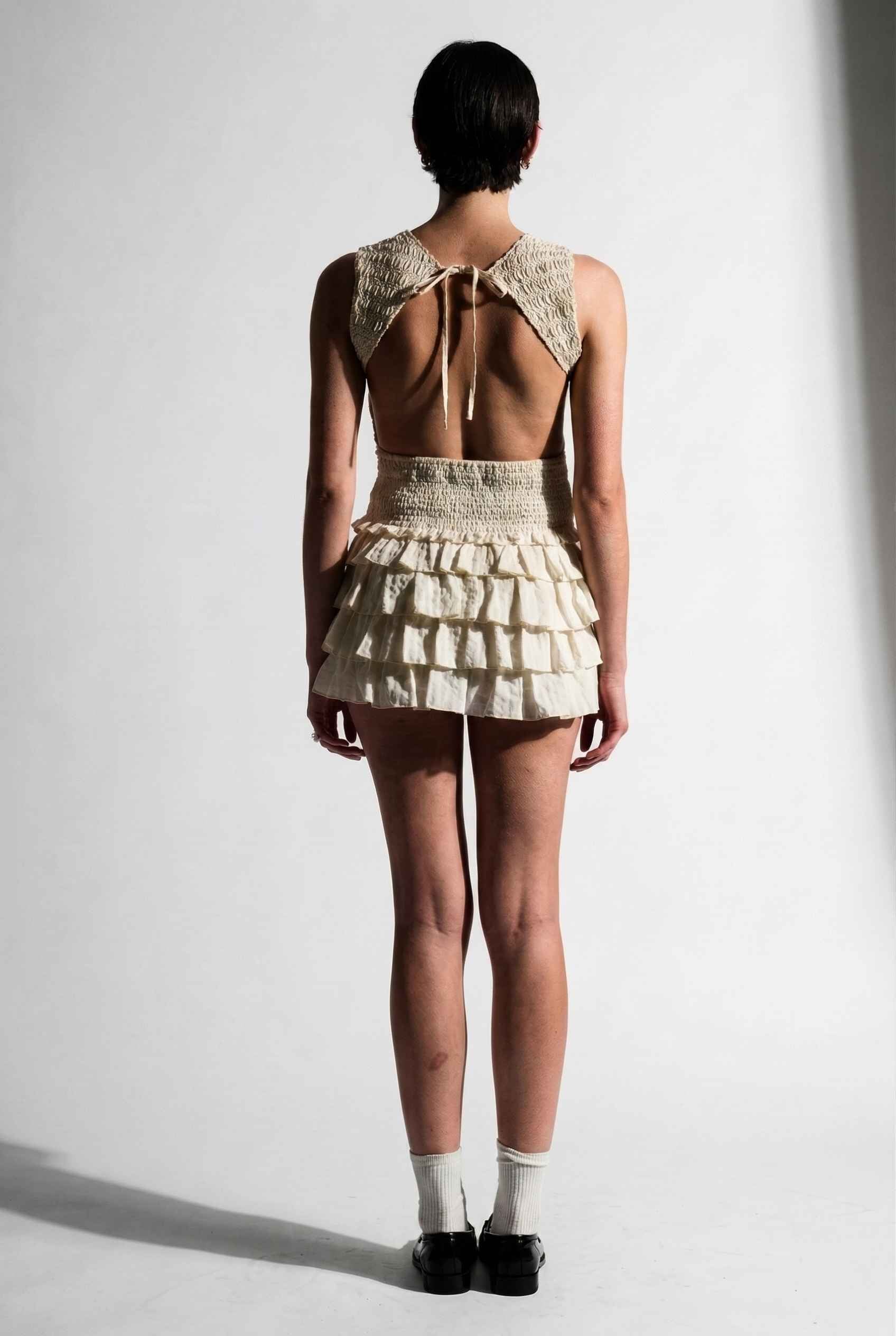 Model wearing Roxy Skirt Ruffle Ra-Ra Mini Skirt in Cream with matching tank top and shiny loafers with socks
