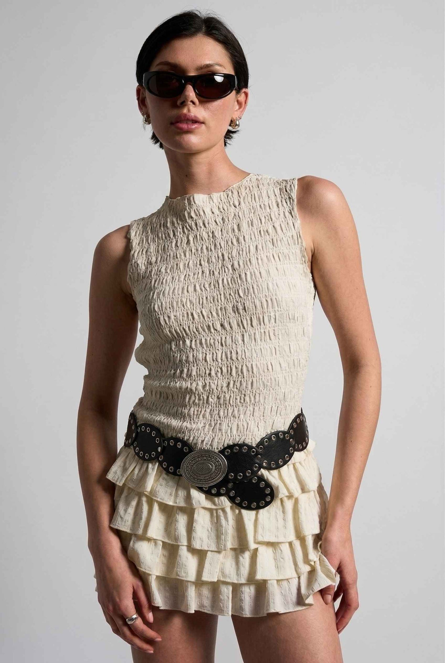 Model wearing Roxy Skirt Ruffle Ra-Ra Mini Skirt in Cream with matching tank top and large buckle belt