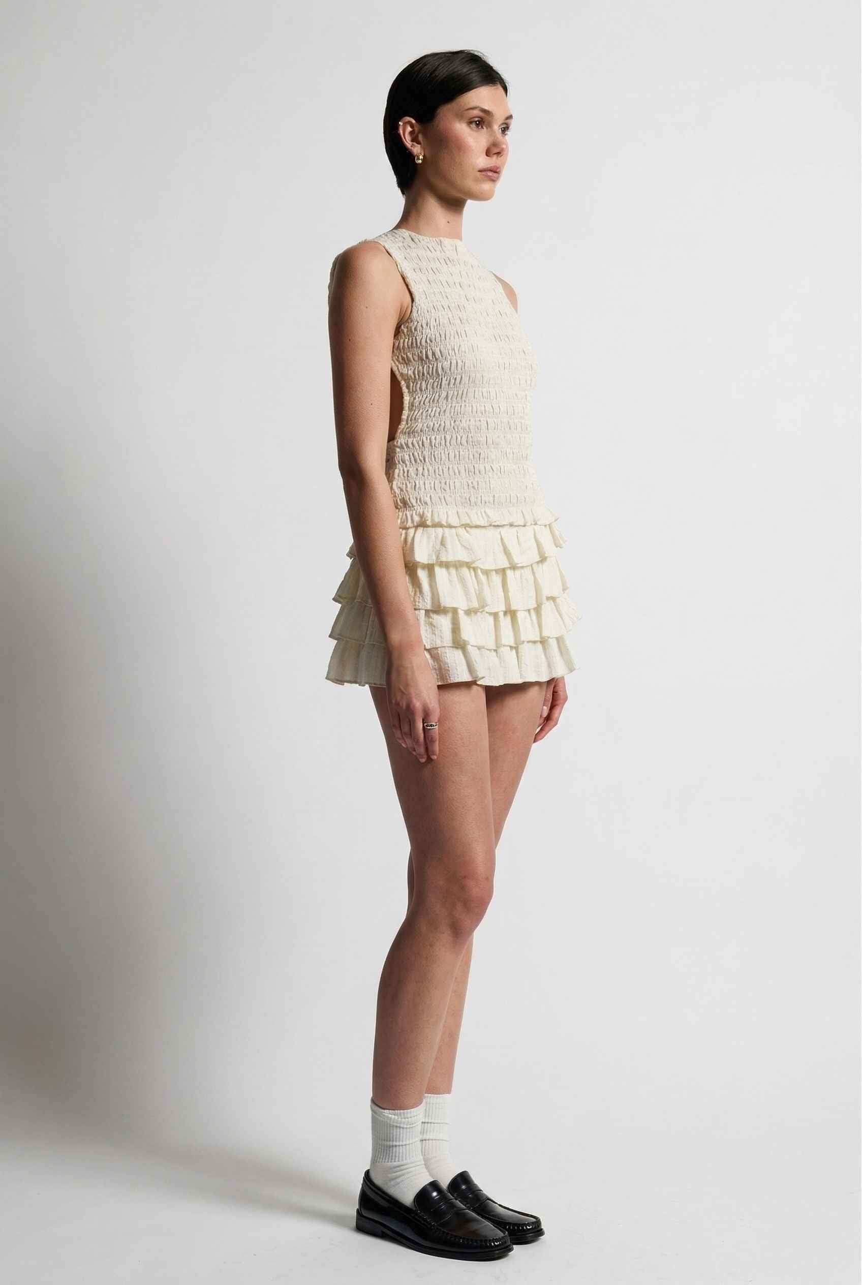 Model wearing Roxy Skirt Ruffle Ra-Ra Mini Skirt in Cream with matching tank top and shiny loafers with socks