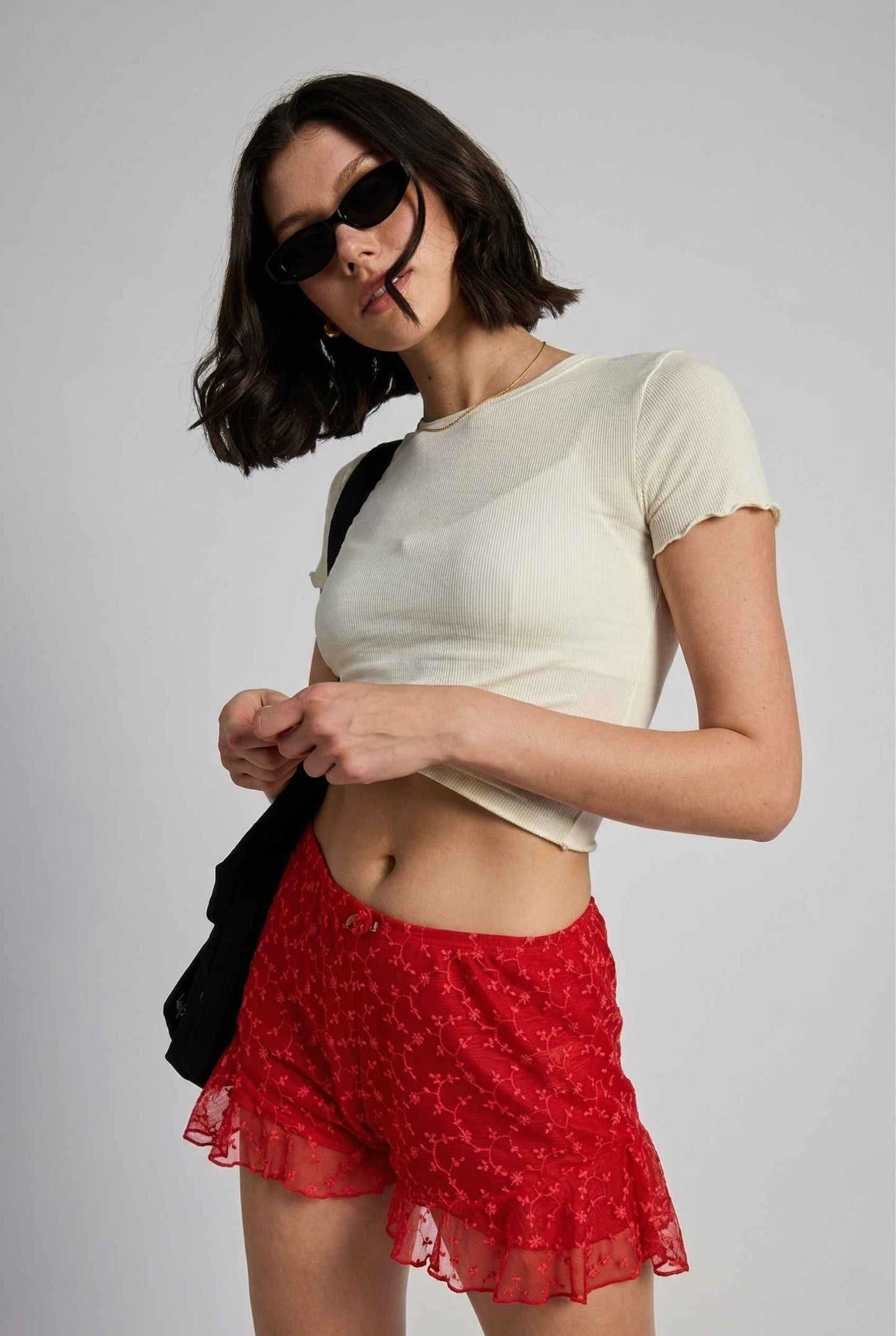 Model wearing Ruby Shorts in Red Lace Ruffle Bloomer Shorts with Bow paired with cropped t-shirt and shoulder bag