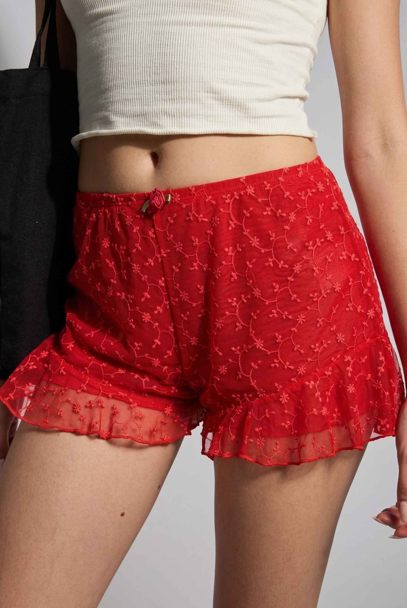 Model wearing Ruby Shorts in Red Lace Ruffle Bloomer Shorts with Bow paired with cropped t-shirt close up delicate lace detail