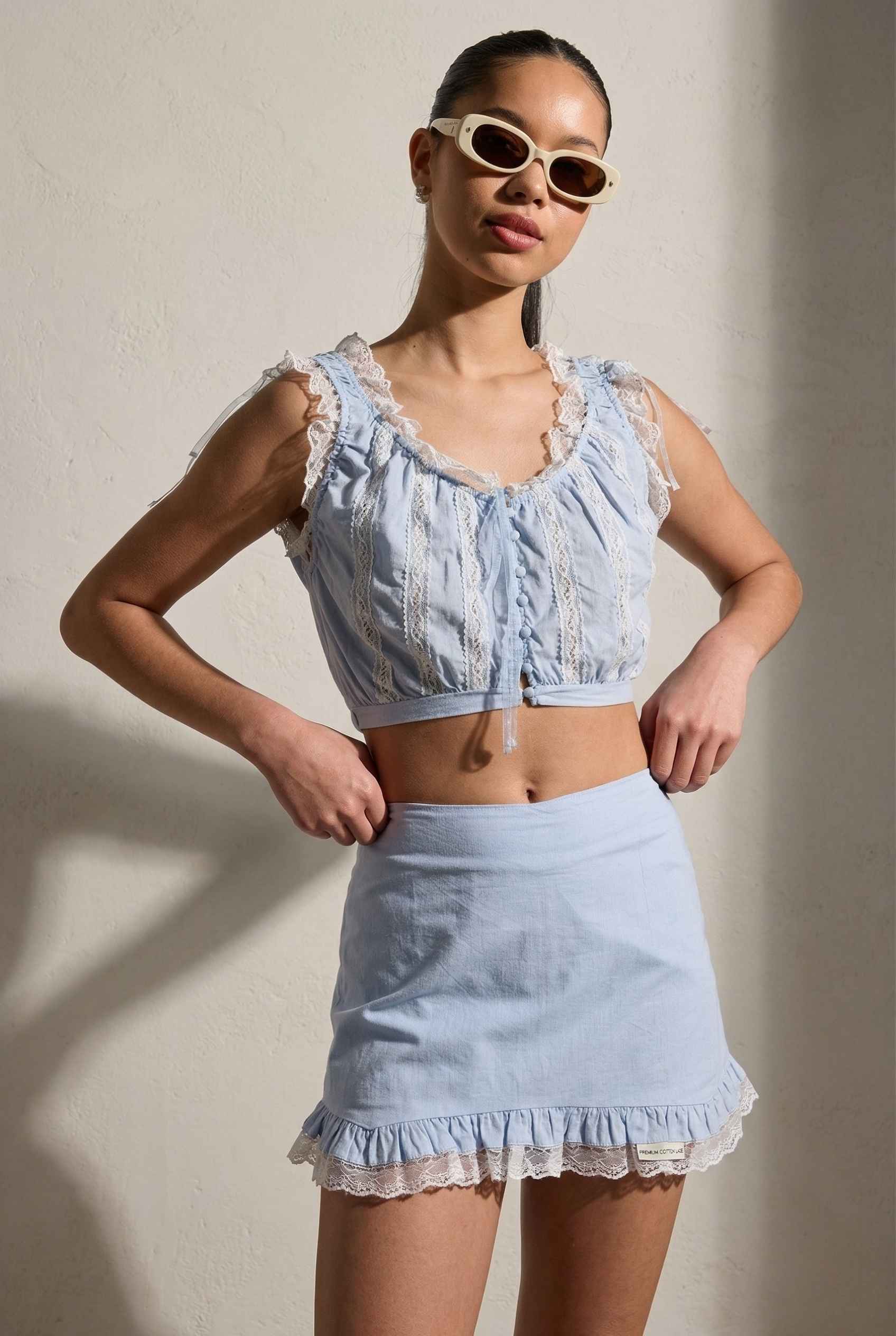 Woman wearing a Seraphina Top Light Blue & White Cotton Lace Ruffle Bralette with ruffled details against a neutral background