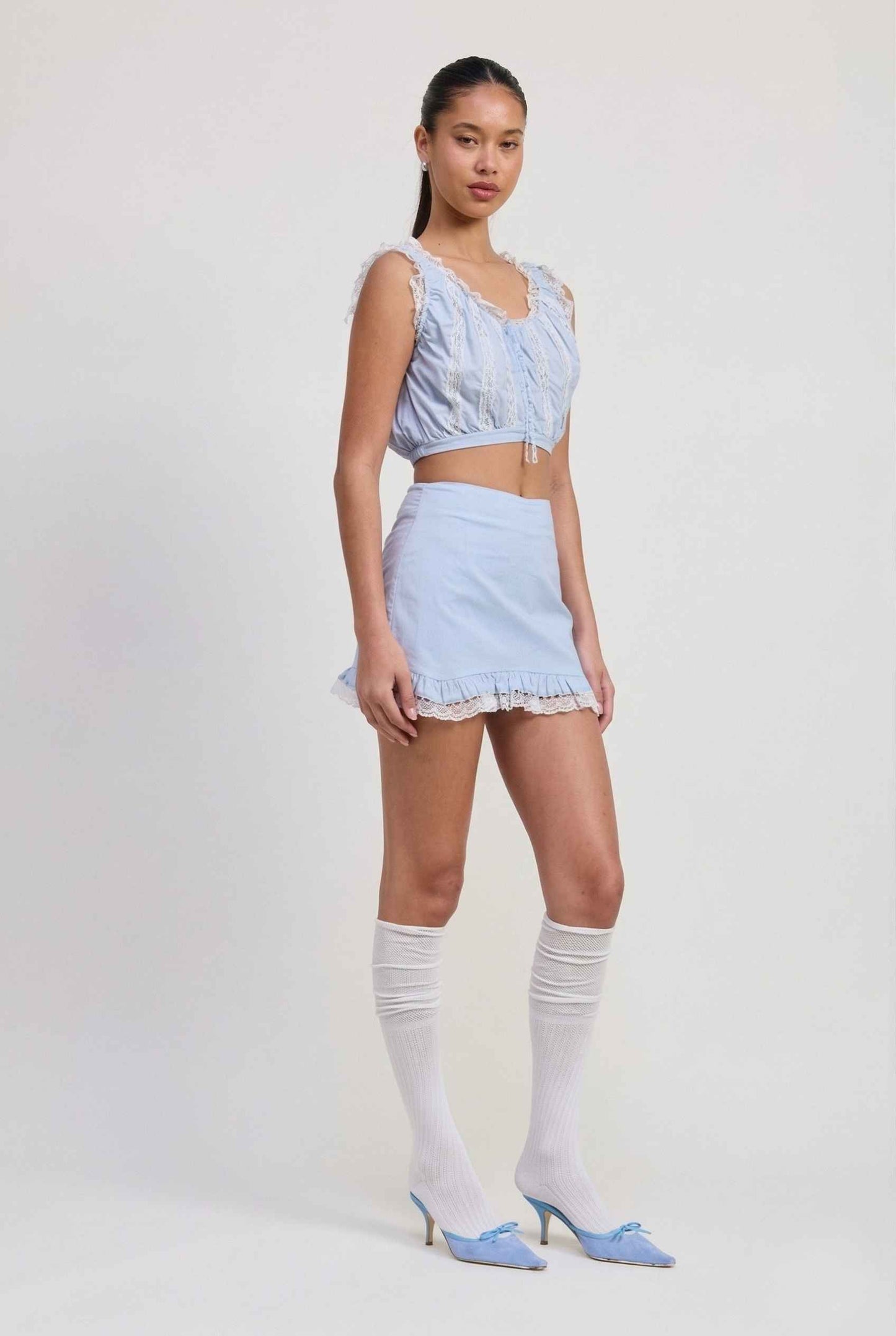 Woman wearing a Seraphina Top Light Blue & White Cotton Lace Ruffle Bralette with matching knee-high socks on a white background