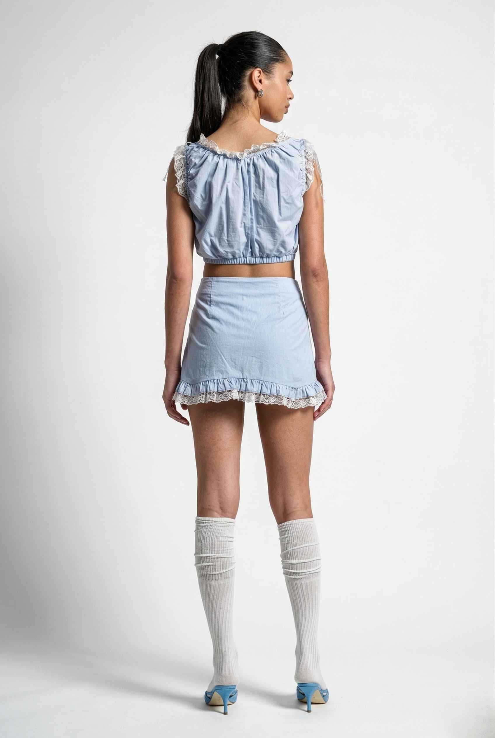 Woman wearing a Seraphina Top Light Blue & White Cotton Lace Ruffle Bralette with knee-high socks on a white background