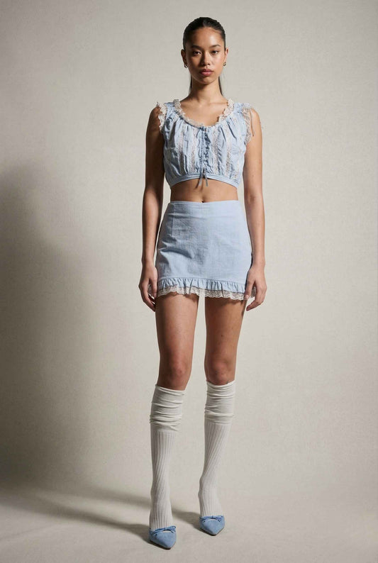 Woman wearing a lSeraphina Top Light Blue & White Cotton Lace Ruffle Bralette and skirt with knee-high socks against a plain background
