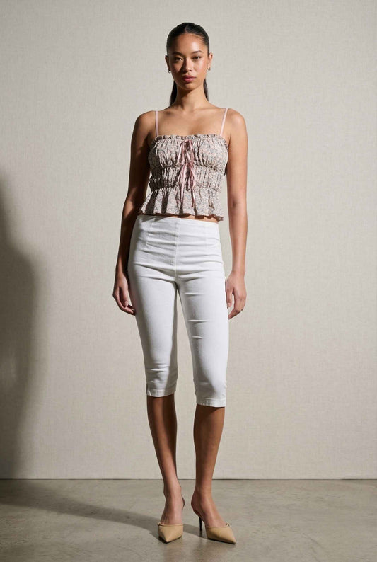 Woman wearing a Seraphina Top Pink Floral Smocked Peplum Cami with Ribbon Ties and white capri pants against a plain background