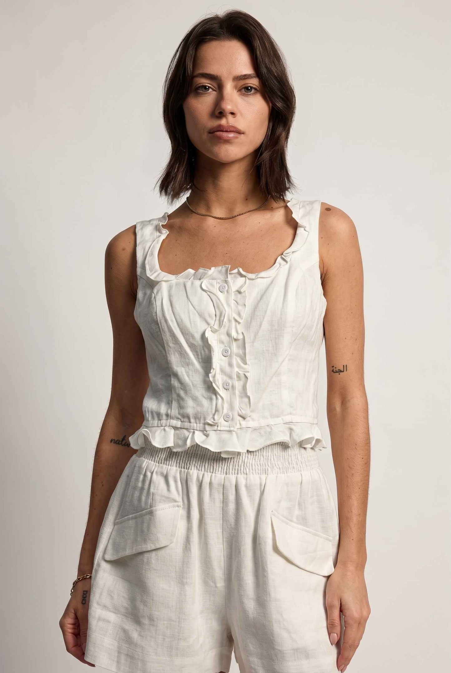 Model wearing Shay Ruffle Button-Front Top Cotton-Linen Tank Top in Off White with matching smocked shorts