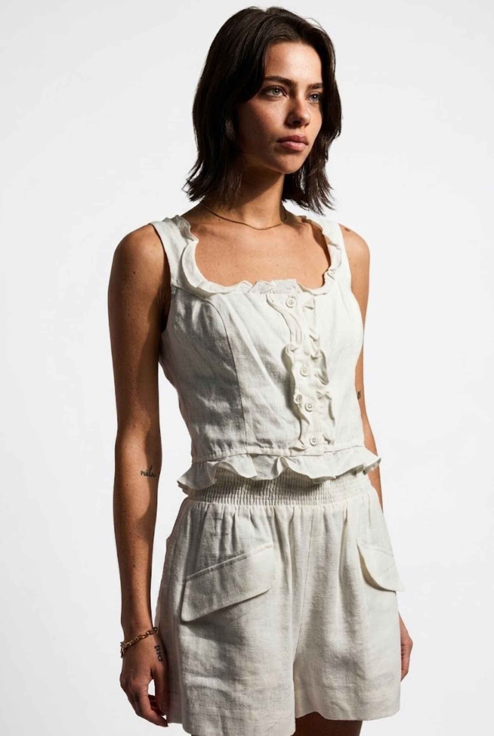 Model wearing Shay Ruffle Button-Front Top Cotton-Linen Tank Top in Off White with matching smocked shorts