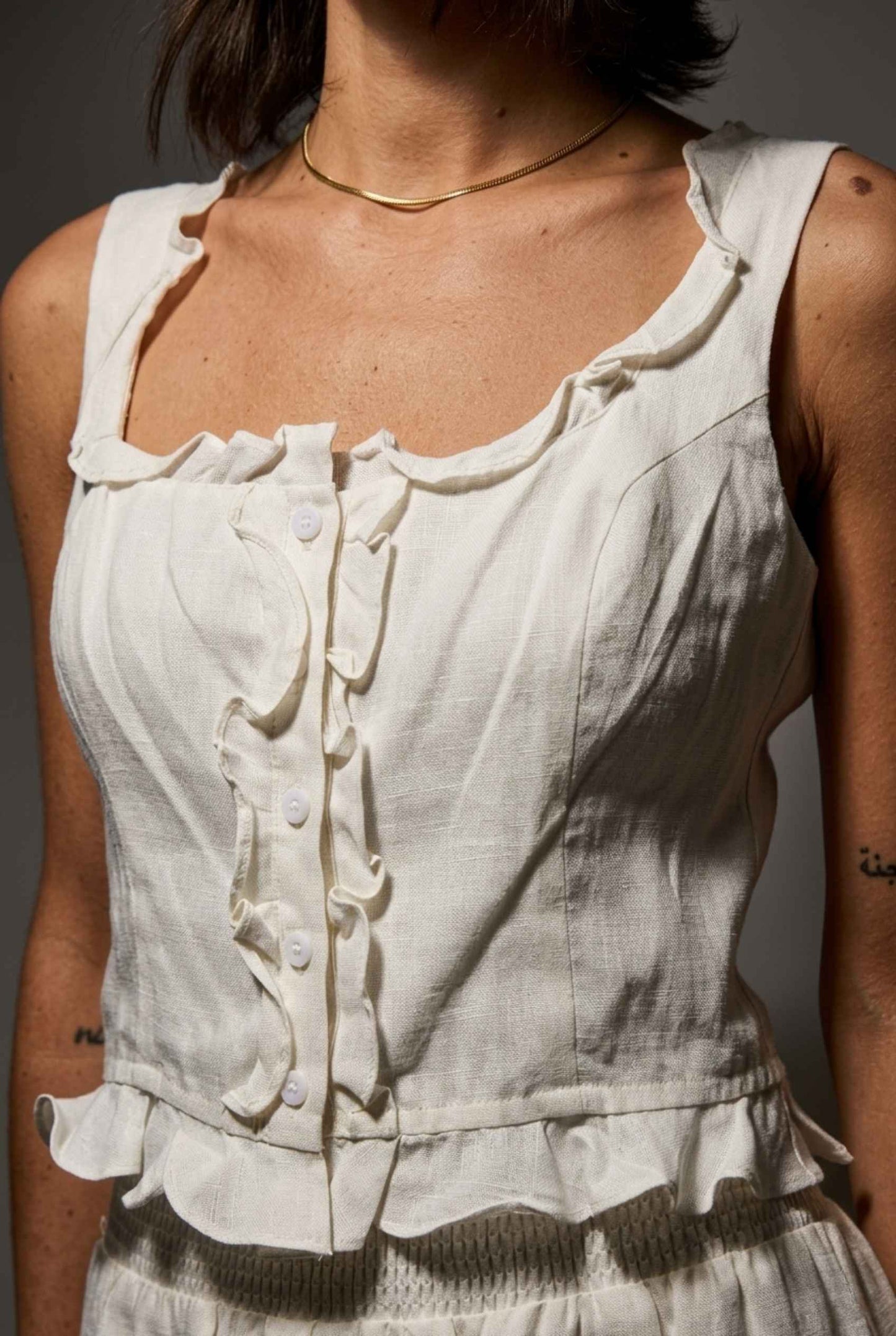 Model wearing Shay Ruffle Button-Front Top Cotton-Linen Tank Top in Off White with matching smocked shorts close up ruffle trim detail
